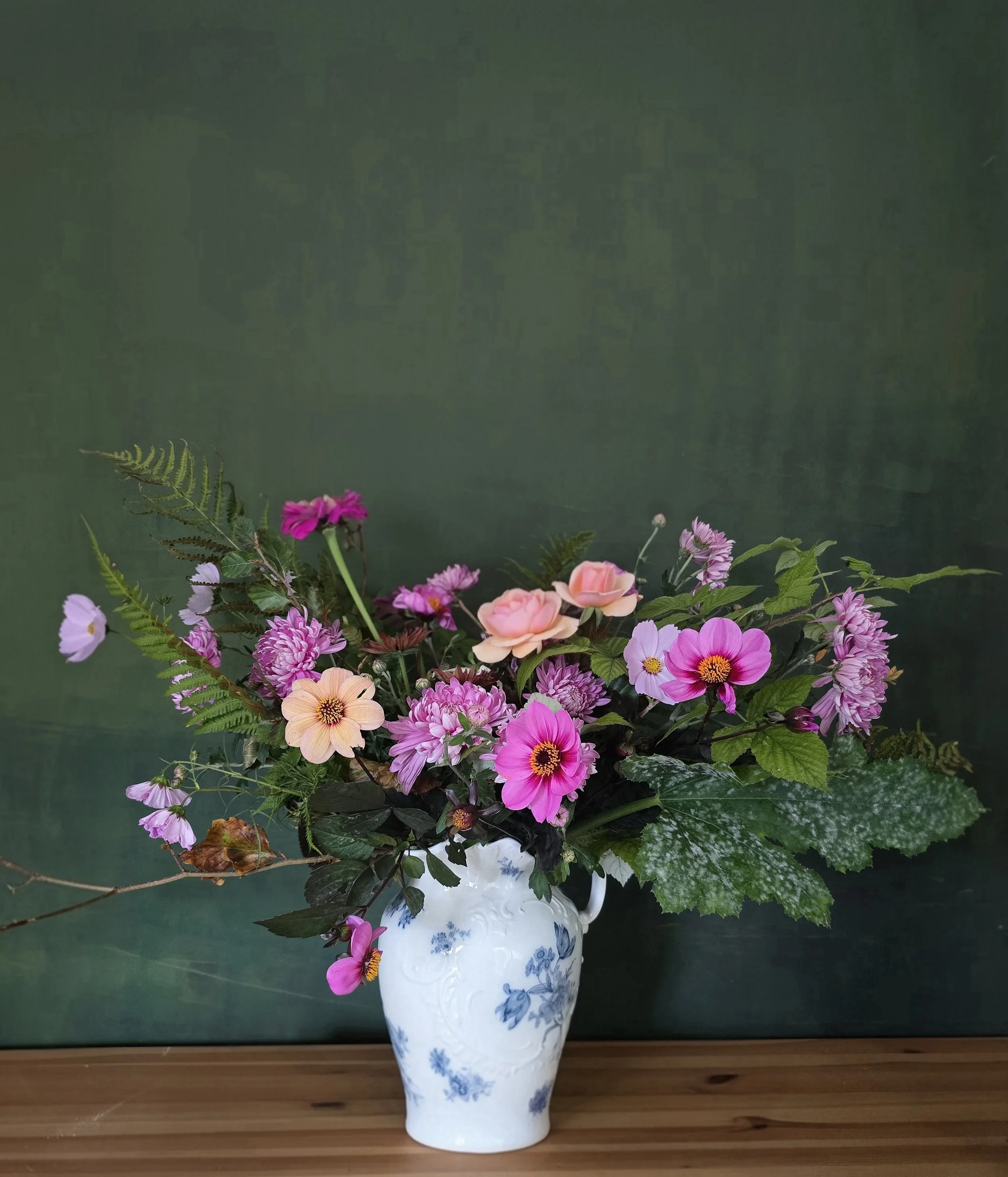 Pink autumn flowers in a white jug with green background.