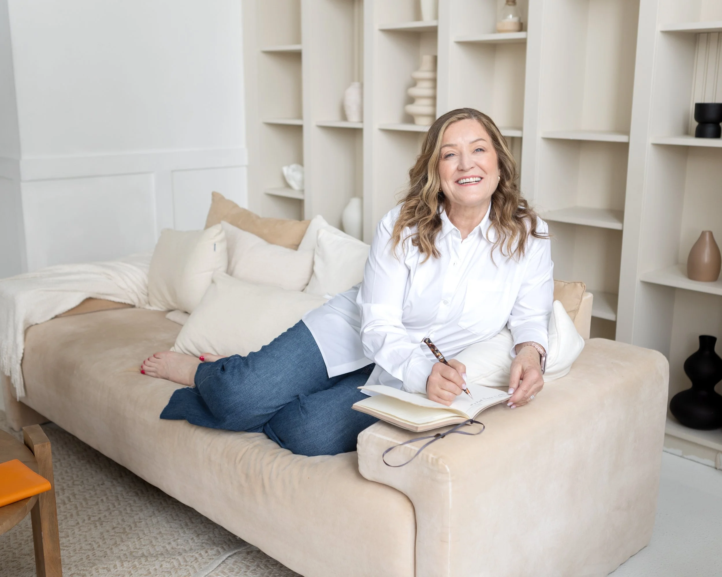 A photo of executive coach Jo Ann Miele sitting on a couch, smiling, with an open notebook on the armrest