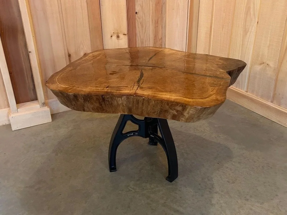 Sample live-edge wooden table with a natural irregular shape, supported by a black metal stand.
