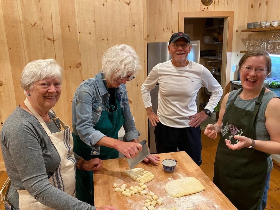 Four people in a kitchen cooking together, with cut pieces of dough on the table.