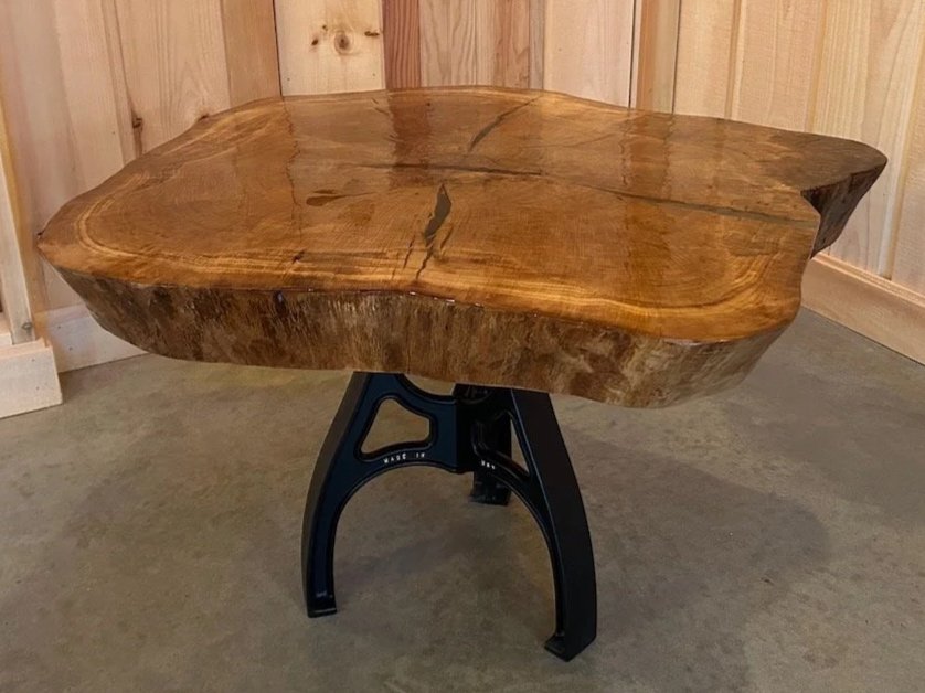 A live-edge wooden table with a black metal tripod-style base.