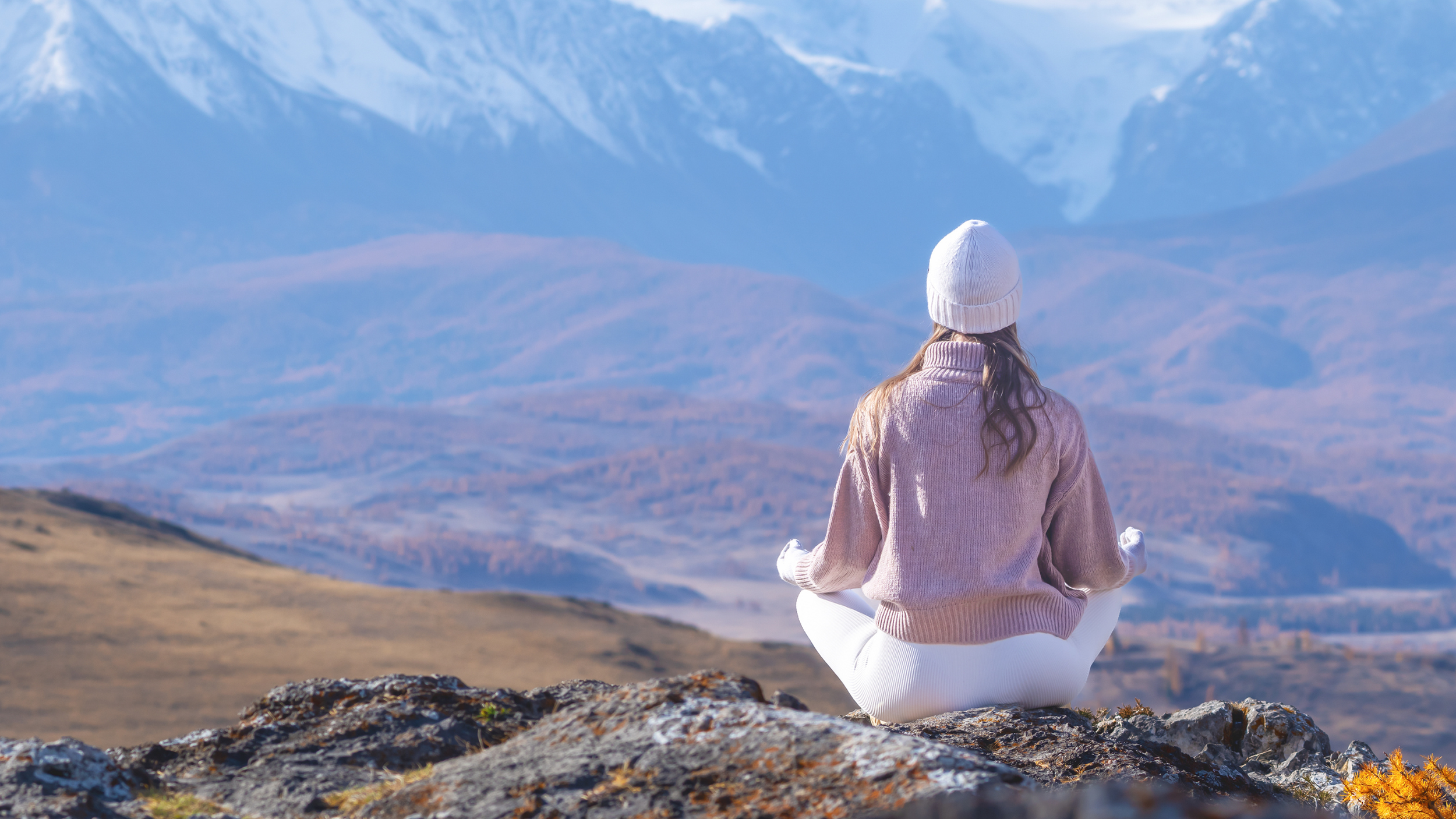 A women in a jacket meditating outside with the mountains