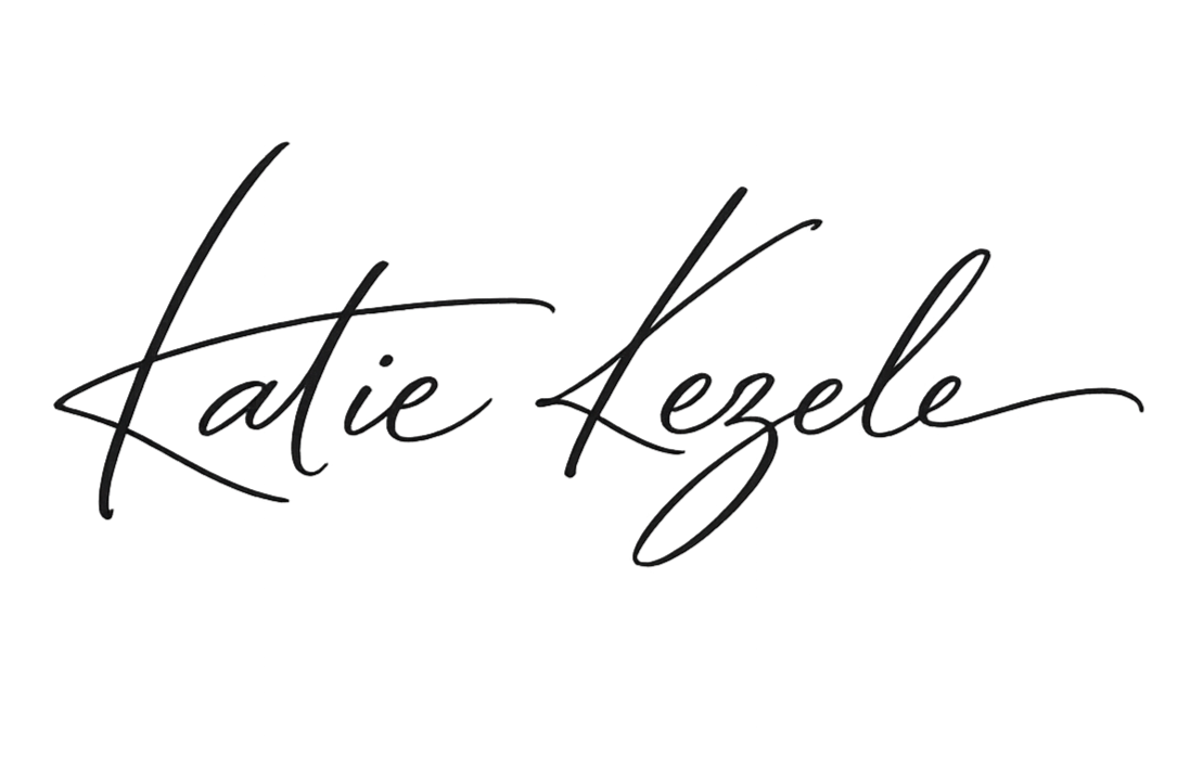 Black cursive signature reading 'Katie Lezele' on a white background.