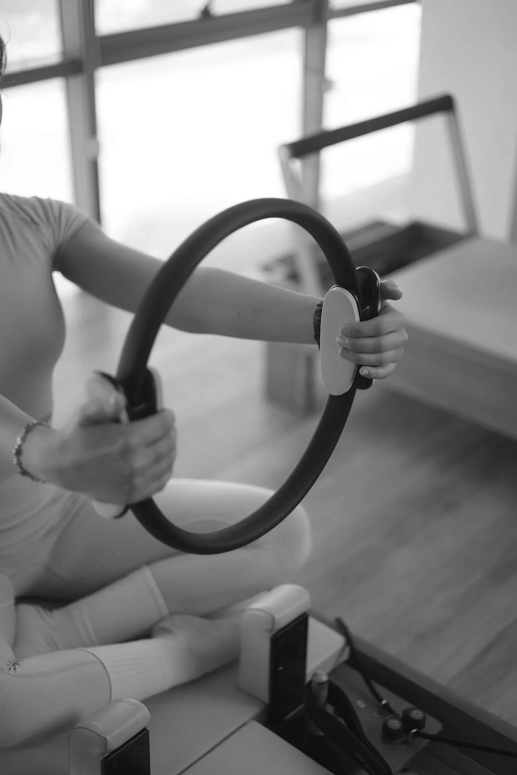 Person sitting in a medical or therapy setting, holding a steering wheel-like device, with medical or therapy equipment visible in the environment.