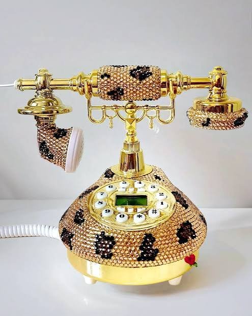 A vintage rotary telephone decorated with pink beads and black floral patterns, featuring gold accents and a small red heart detail.