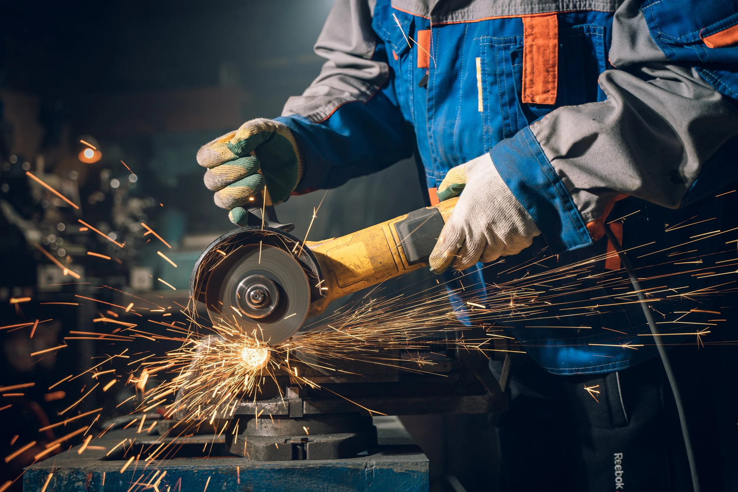 Close-up of a worker grinding metal with an angle grinder, sparks flying, in an industrial workshop.