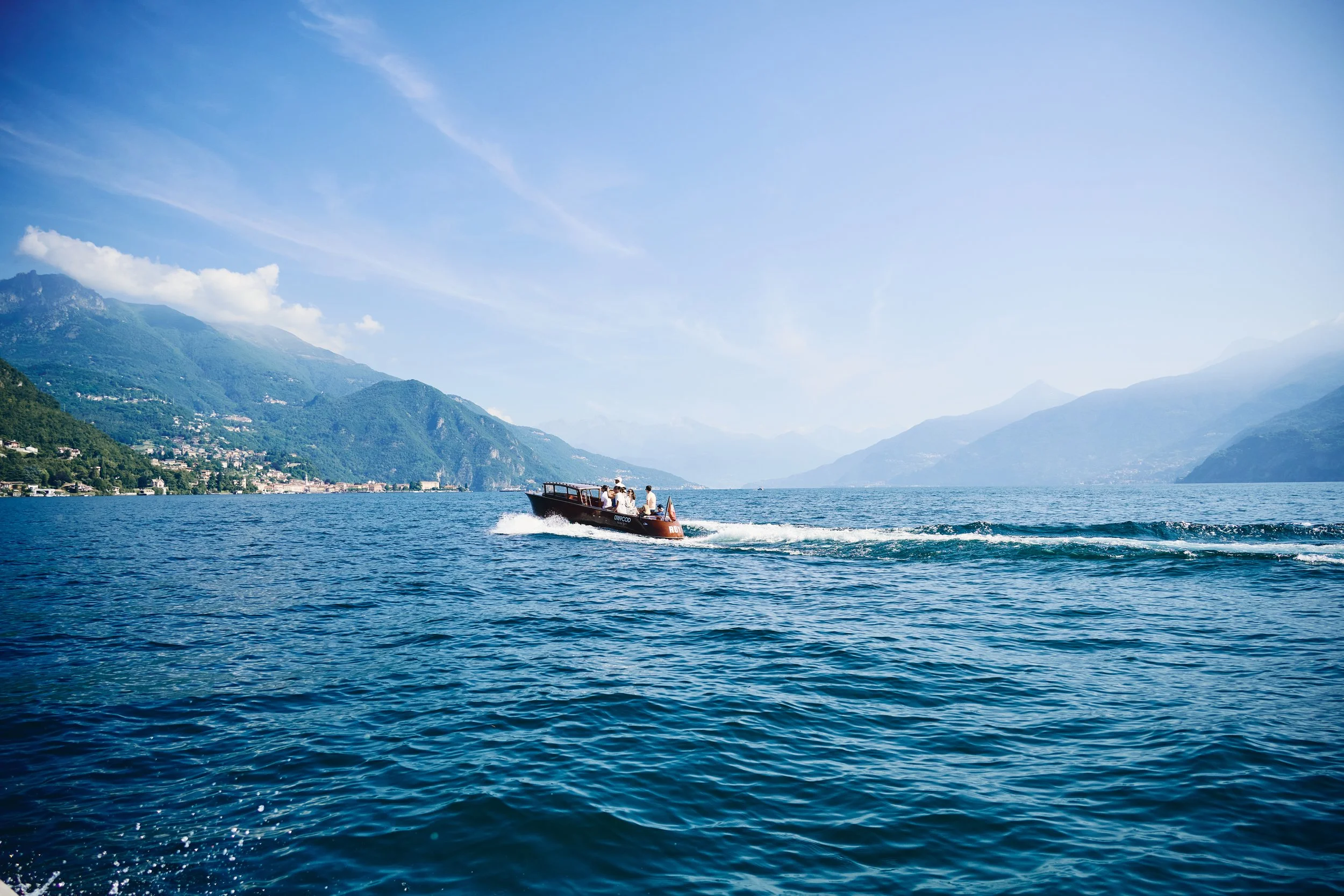 A motorboat moving across a large body of water with mountains in the background under a partly cloudy sky.