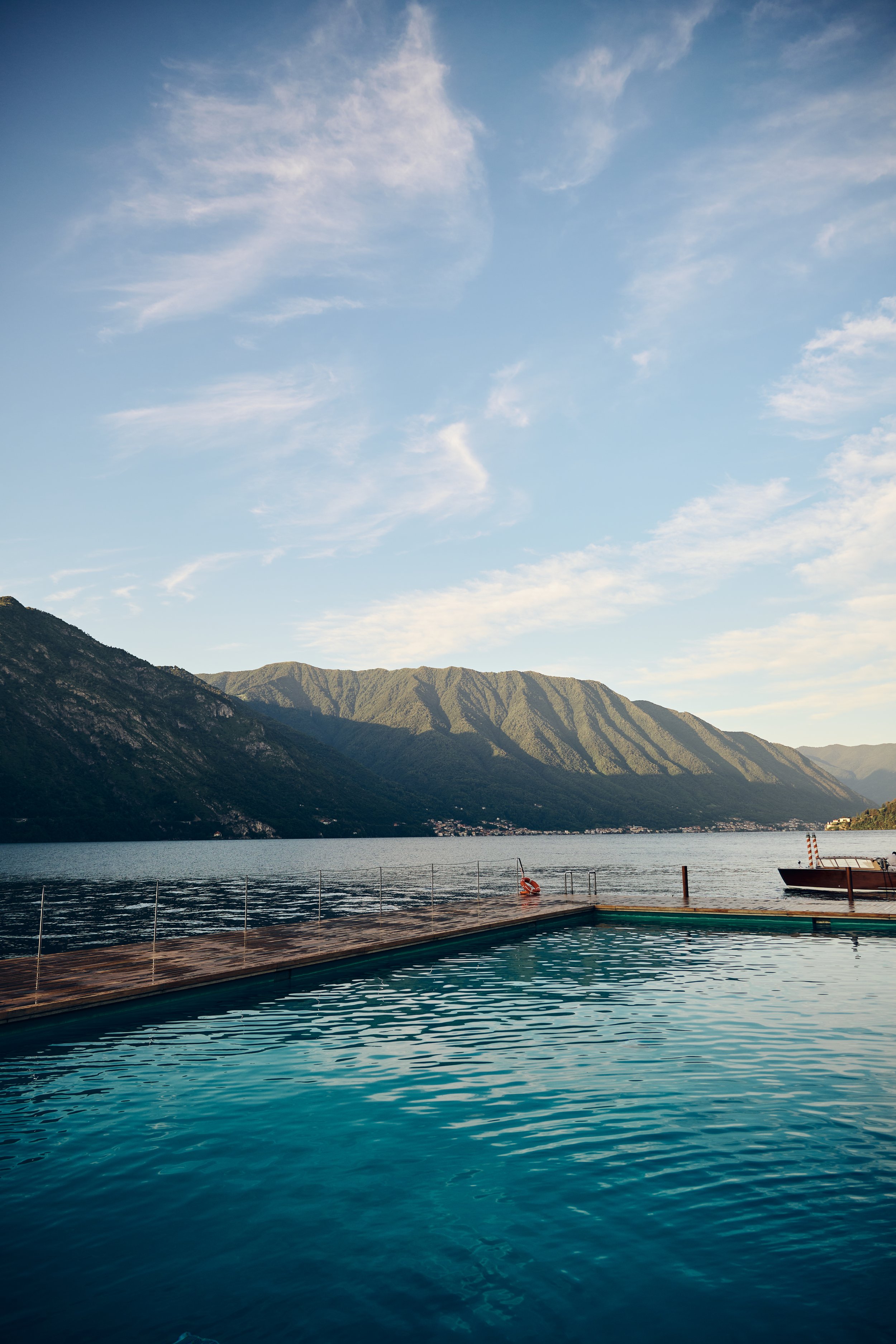 A scenic view of a swimming pool overlooking a body of water with mountains in the background and a clear blue sky.
