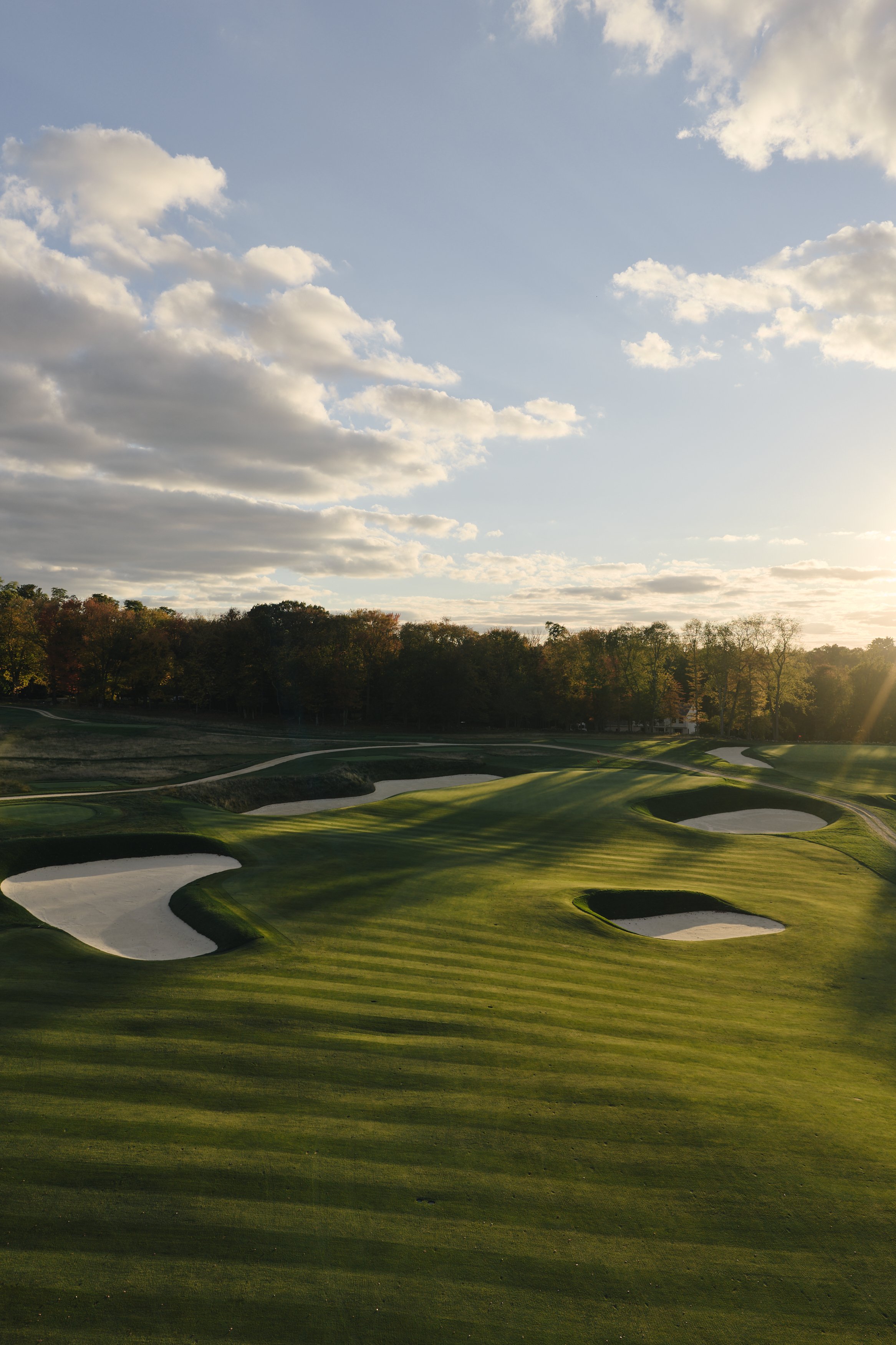 Sunset over a golf course with sand traps and green fairways, framed by trees.