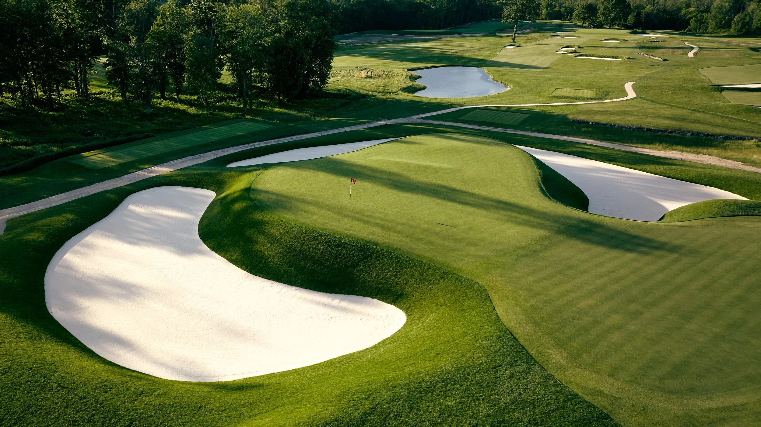 A golf course with green fairways, sand traps, and water hazards, surrounded by trees.