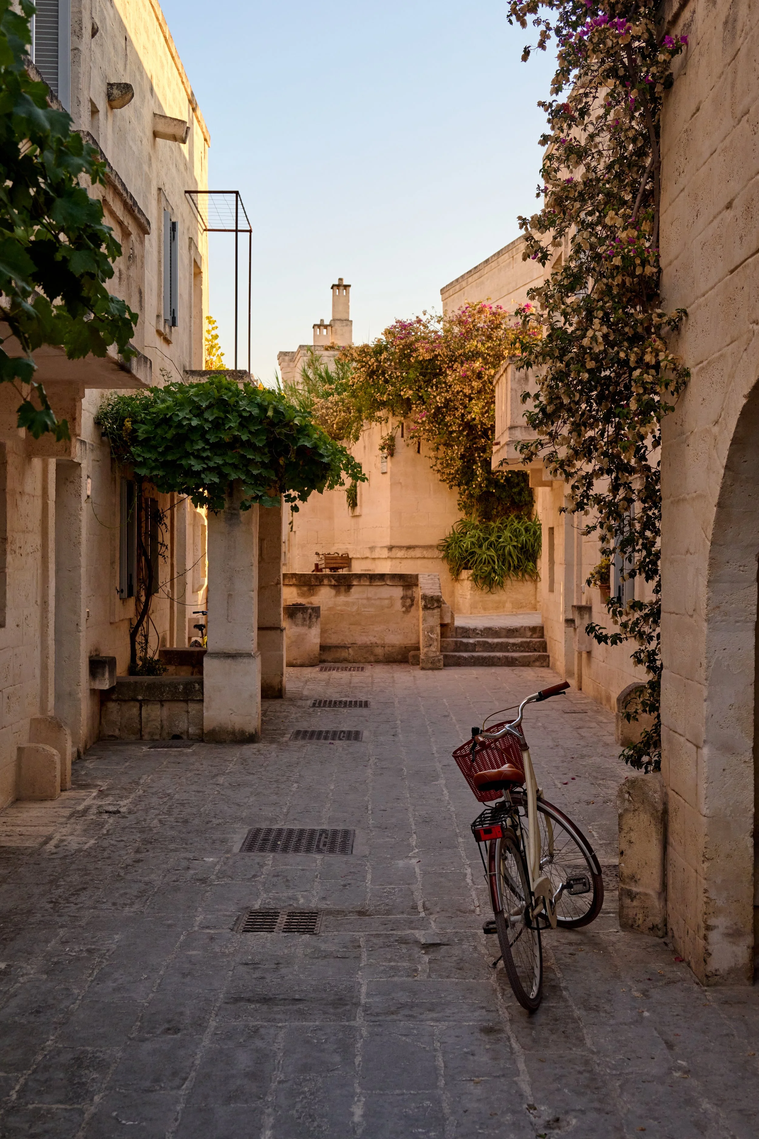 A quiet cobblestone alleyway in a historic European town, with beige stone buildings, creeping plants, and a single bicycle parked on the right side.