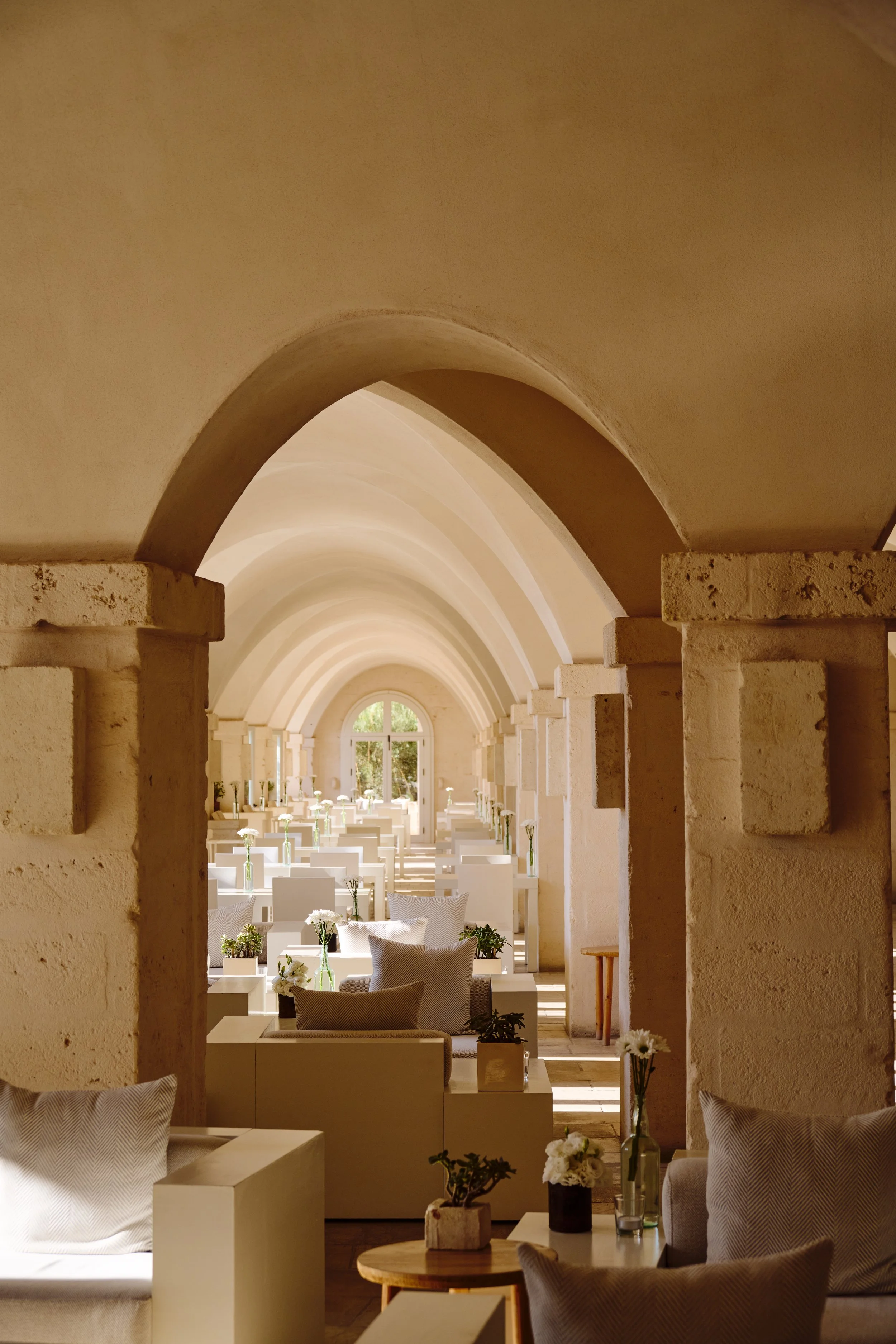 Interior of a bright, modern room with arched ceilings, white furniture, and flower arrangements.