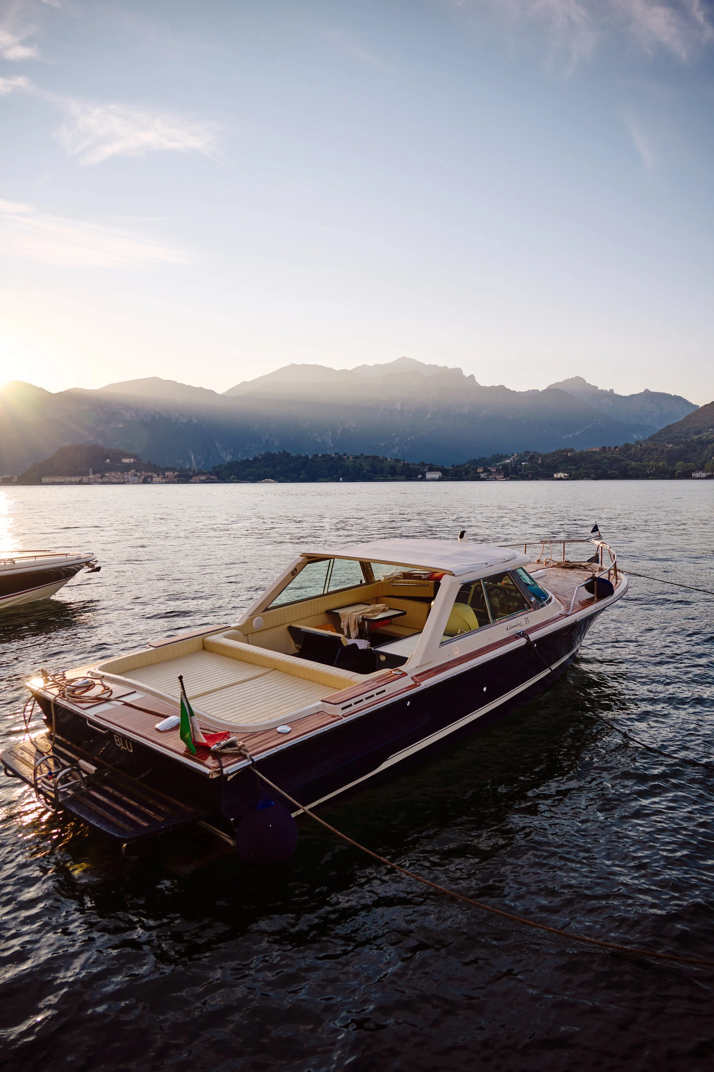 A luxury motorboat docked on a lake with mountain range in the background during sunset.