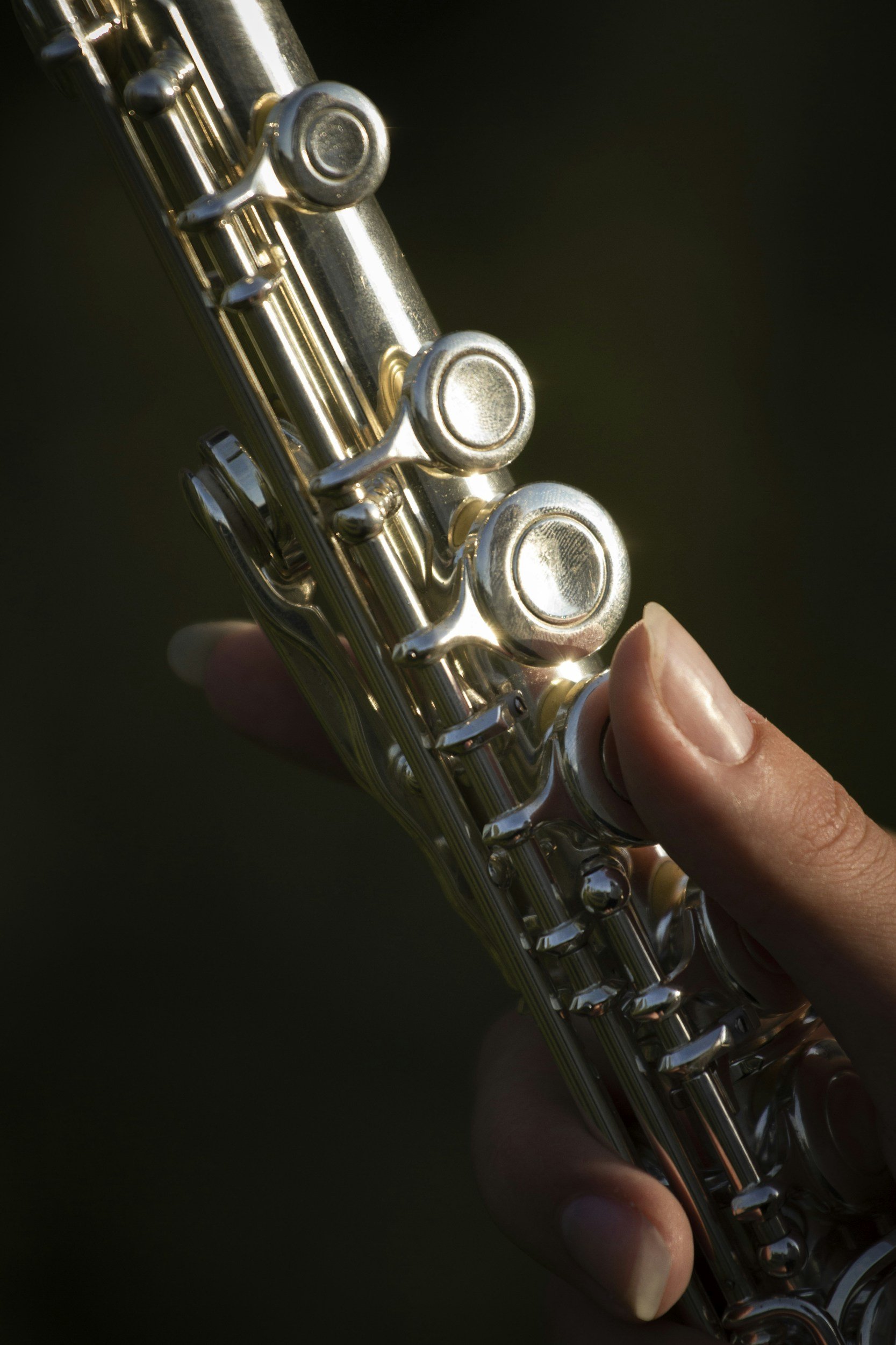 Close-up of a person holding a silver flute, showing the mouthpiece and keys, against a dark background.