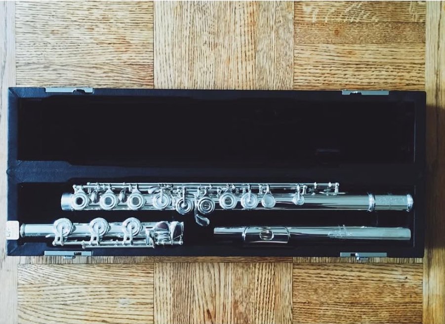 A silver flute inside a black case on a wooden floor.