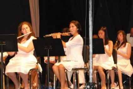 A group of five young women playing flutes on stage during a performance.