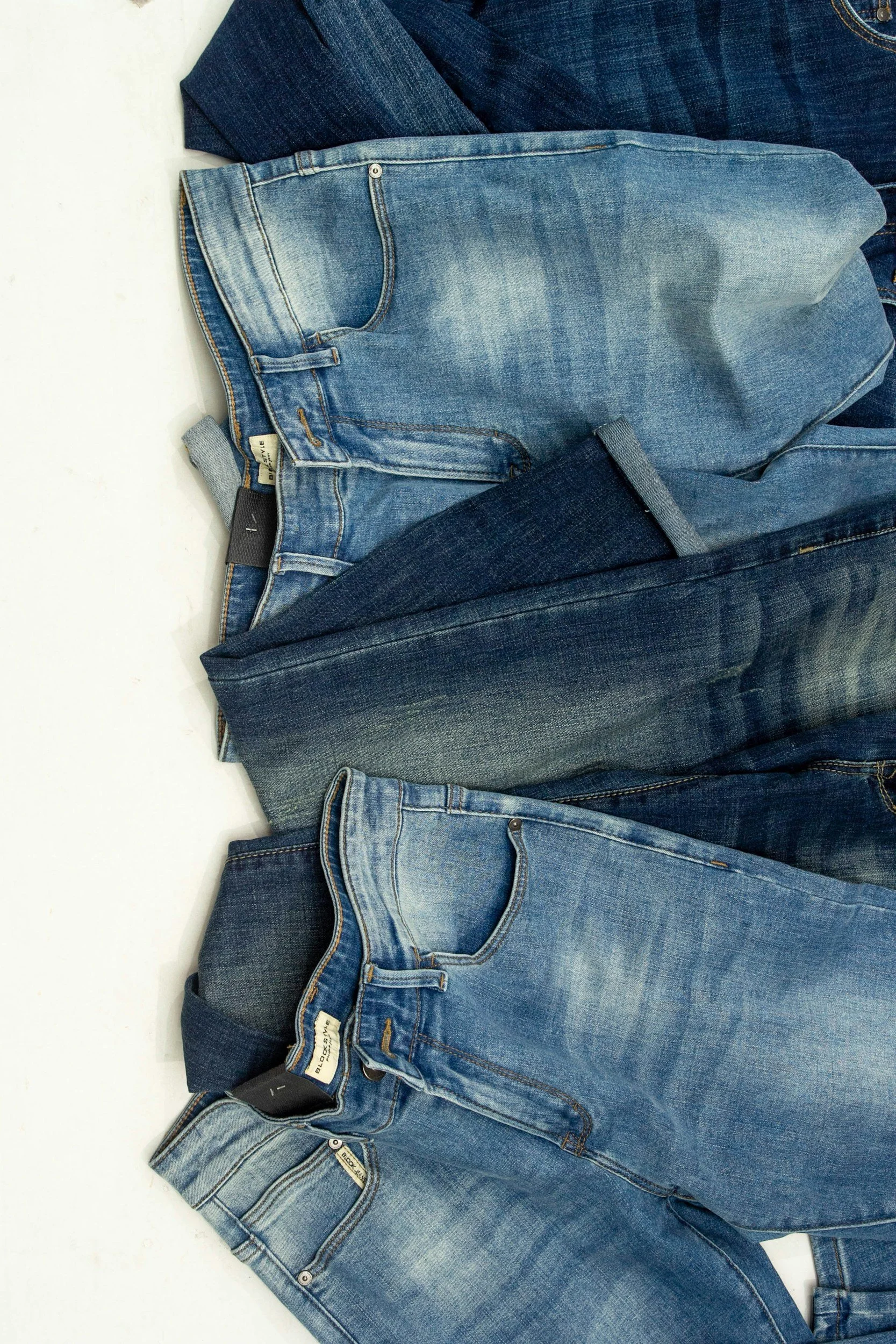 Several pairs of blue denim jeans layered on a white surface, showing different shades and styles.
