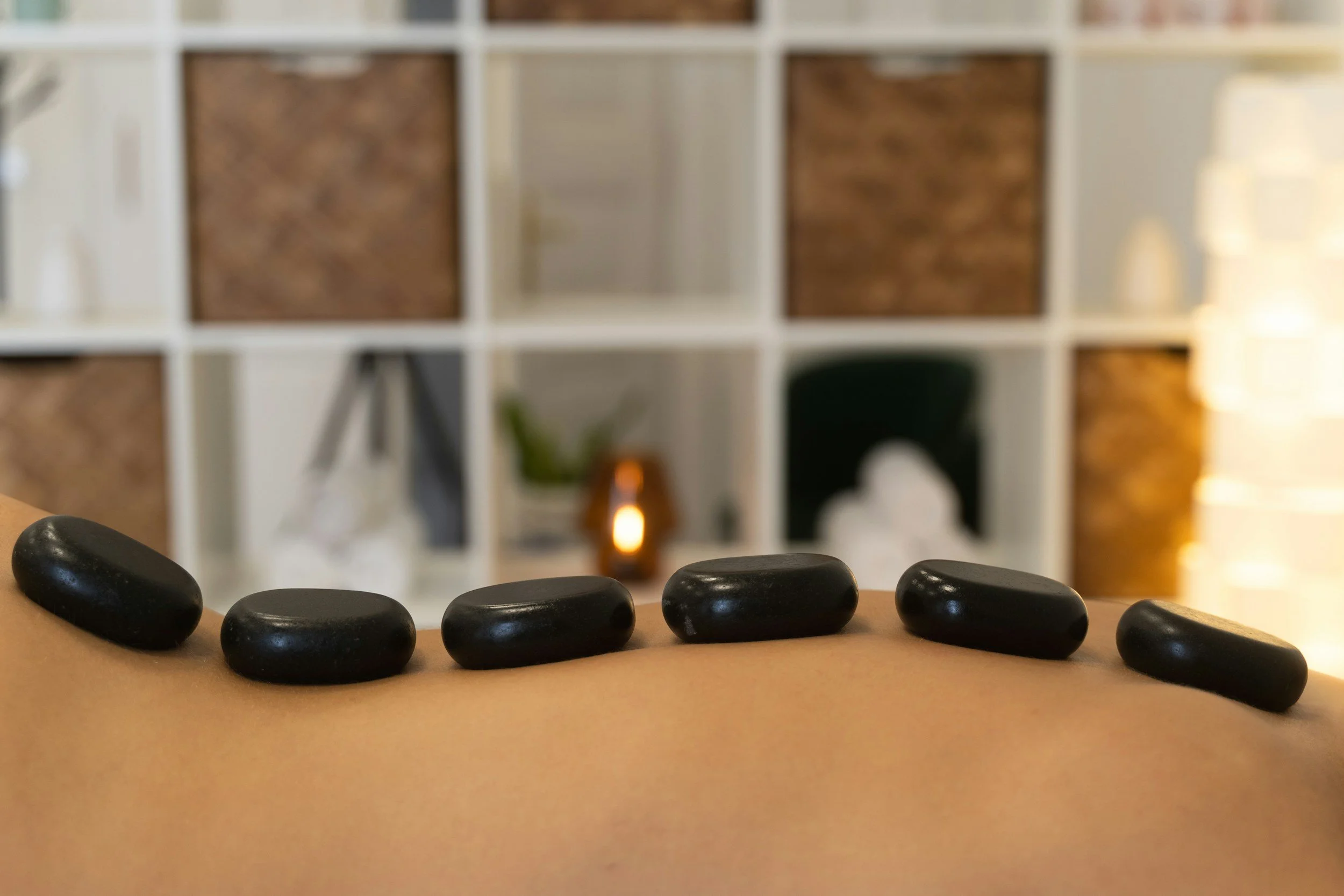 Black stones placed on a table with a blurred background of a white shelving unit and decorative items such as a small plant and a candle.
