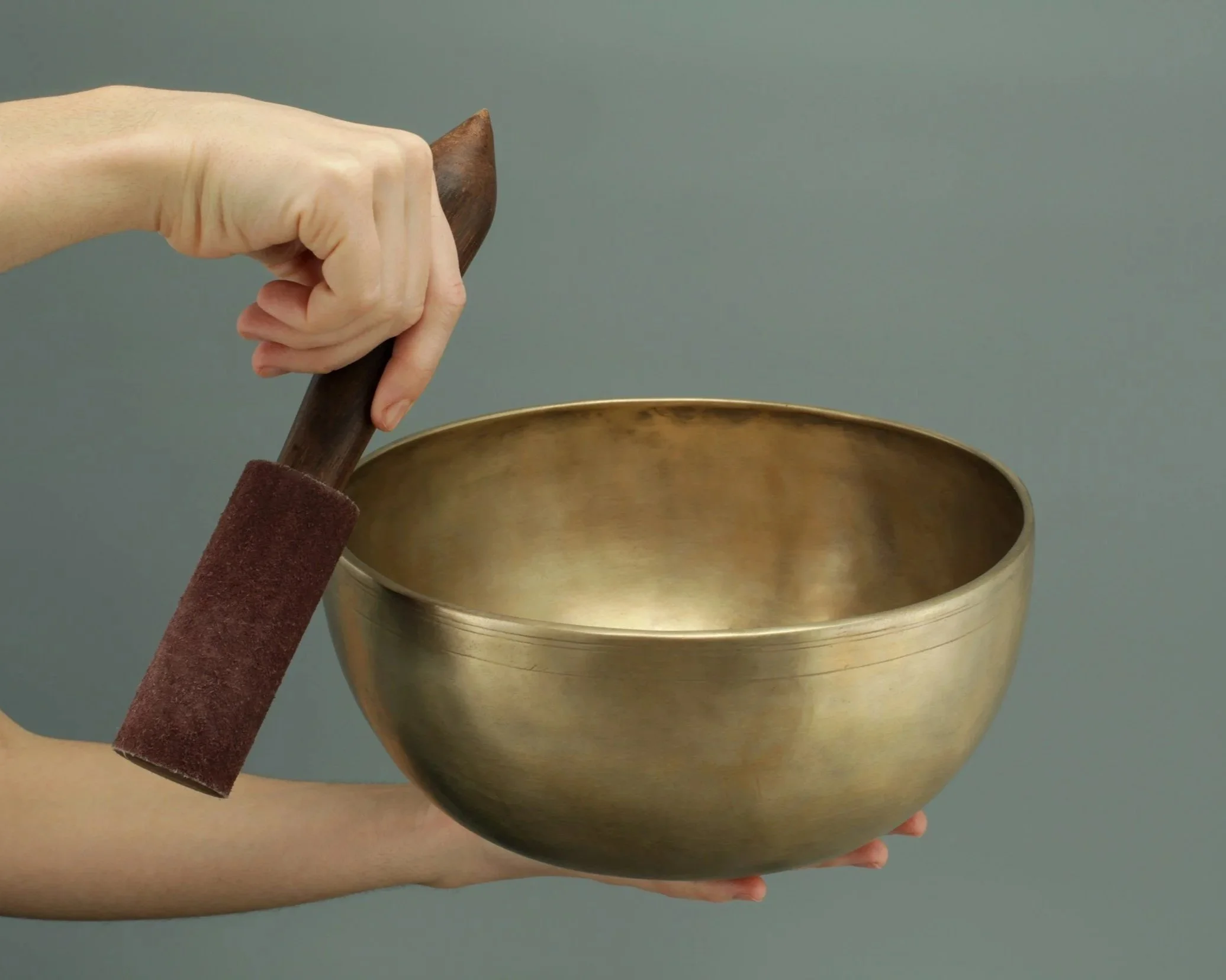 A person holding a wooden mallet over a metallic singing bowl.