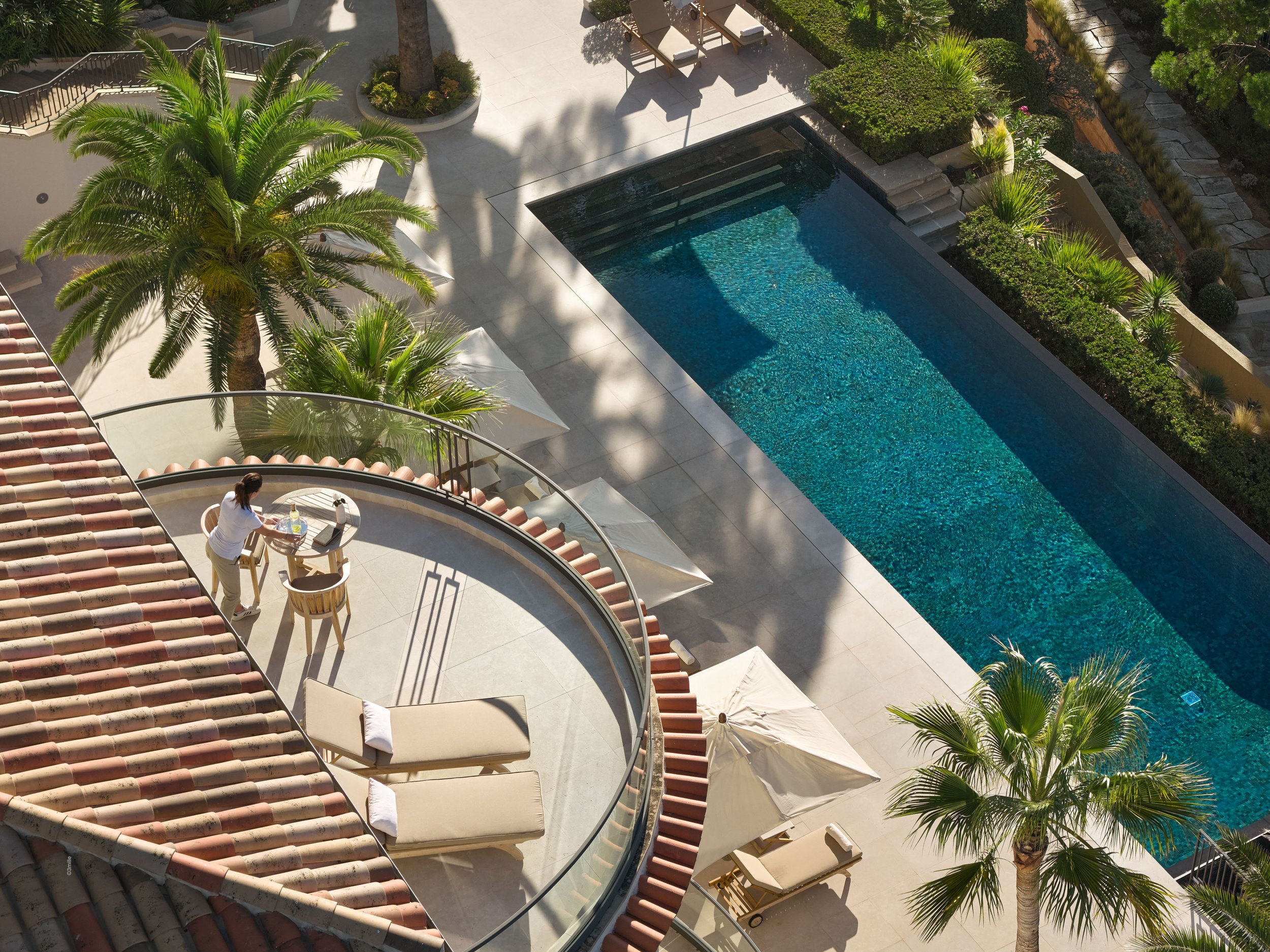 Vue aérienne de la piscine, entourée de végétation, avec des parasols et des chaises longues