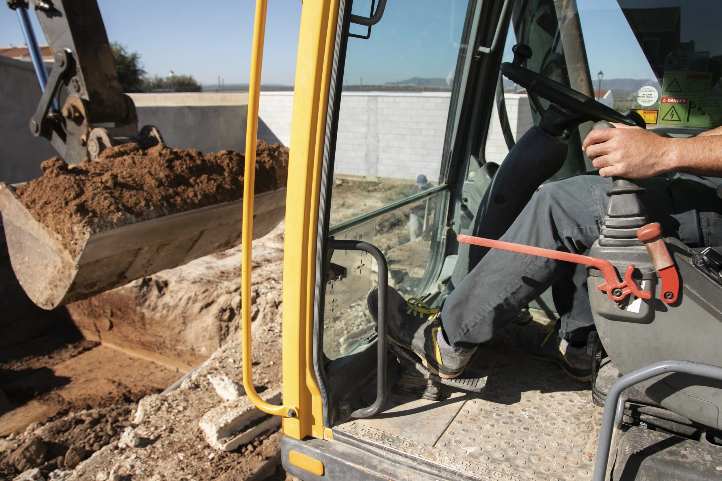 Construction worker operating a small excavator, scooping dirt at a construction site.