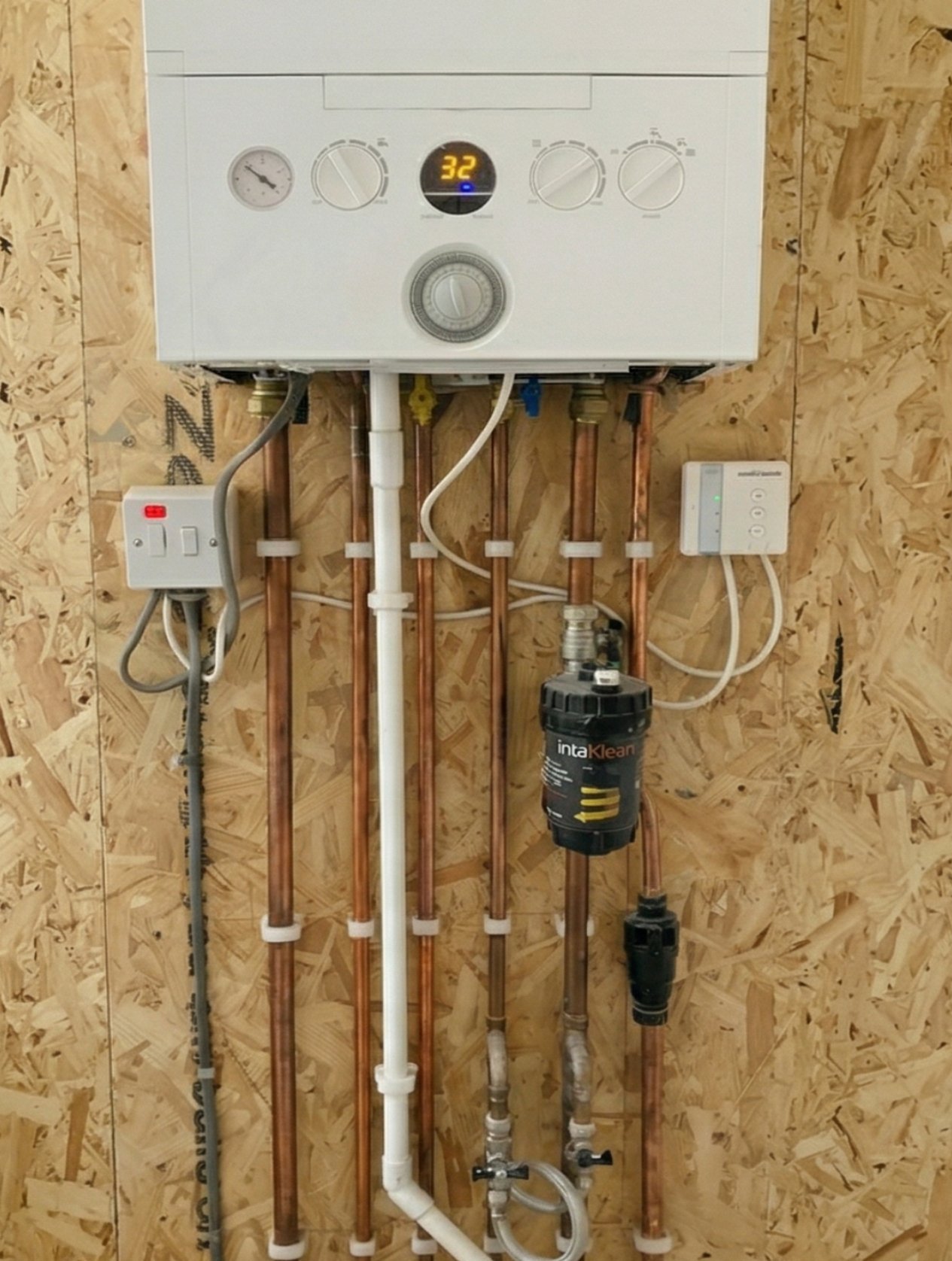 A residential water heater installed on a wooden wall with copper pipes and a water filter.