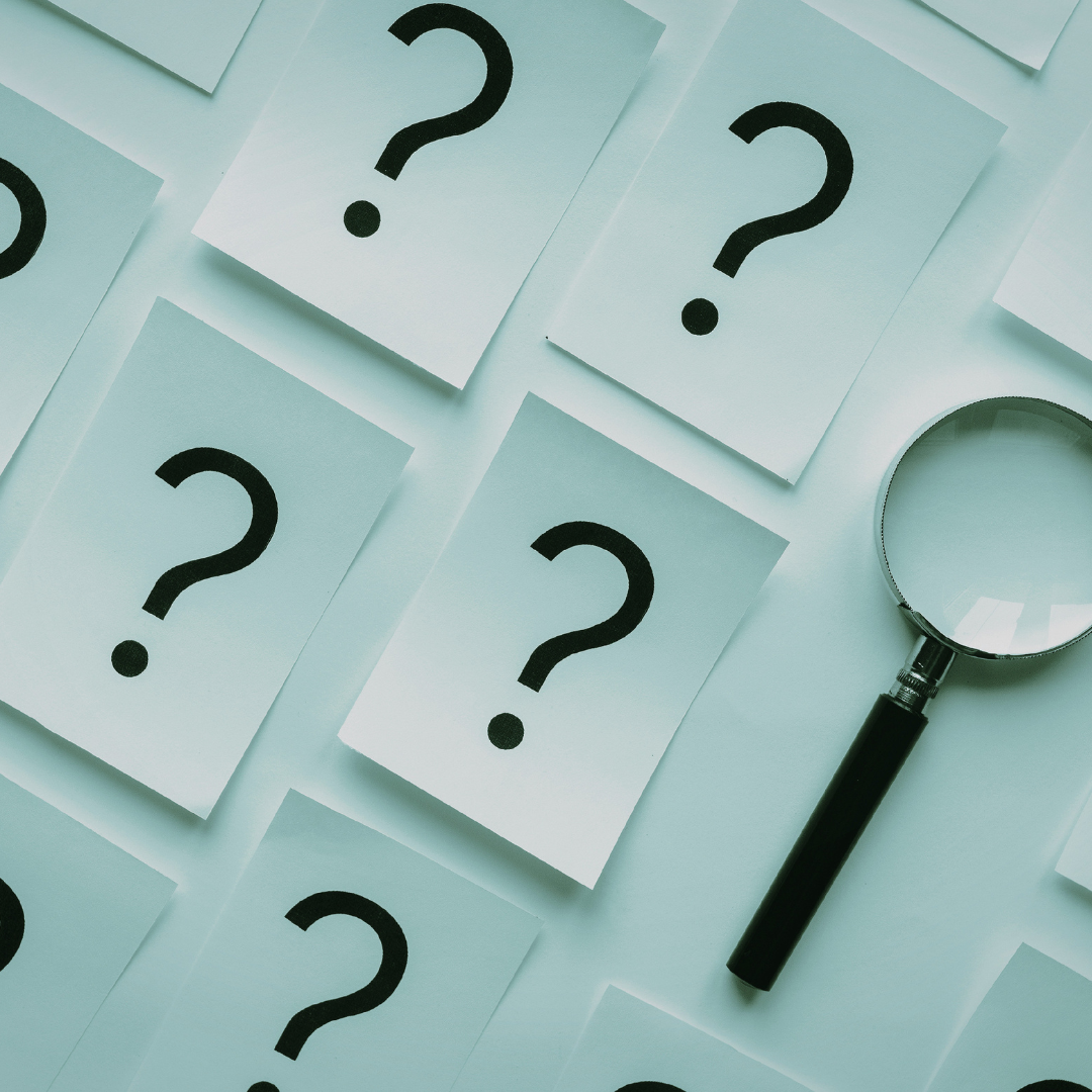Multiple white paper sheets with large black question marks scattered across a light background, with a magnifying glass on the right side.