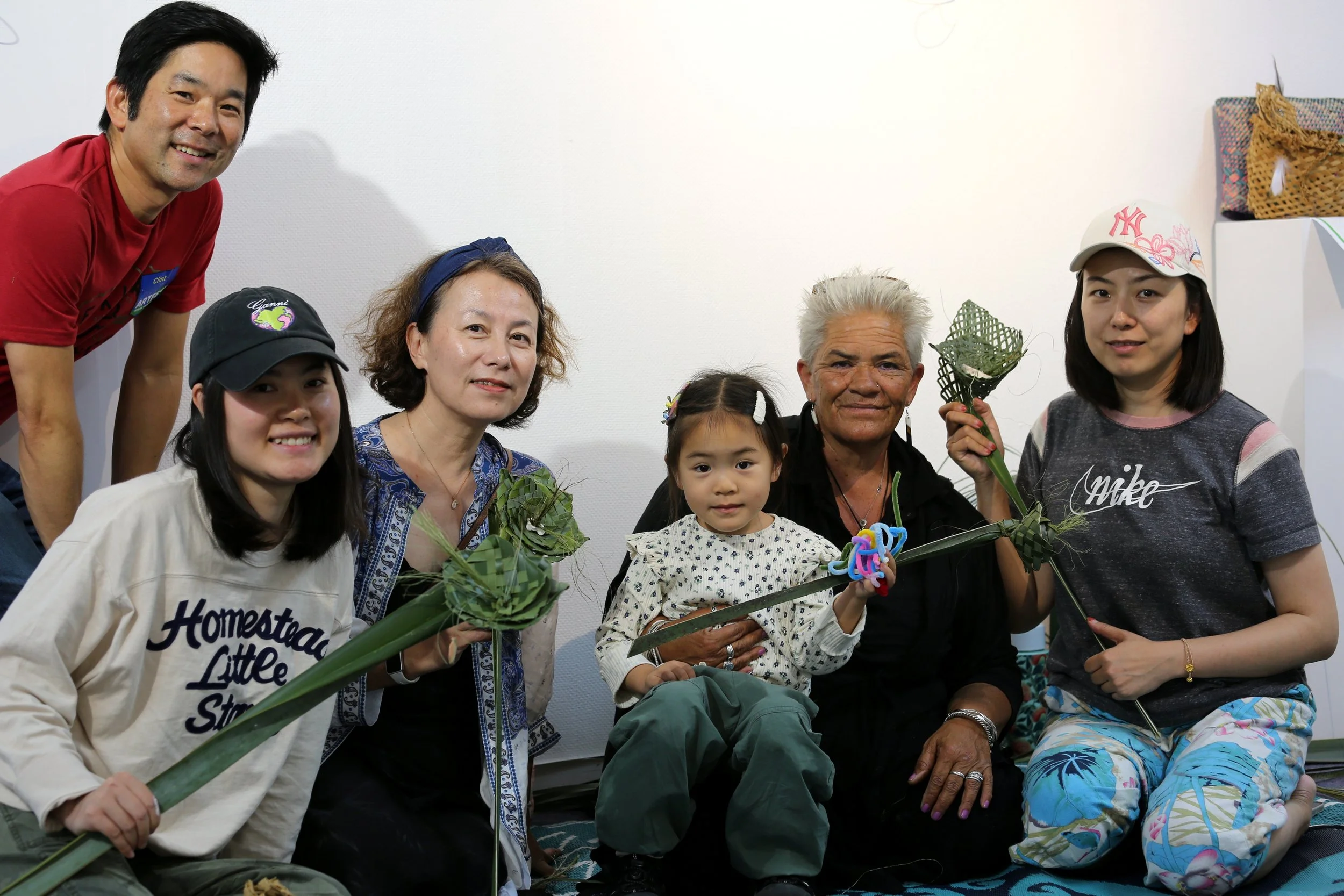 Group of seven people, including three children, gathered indoors, holding woven palm frond crafts, smiling for the photo.