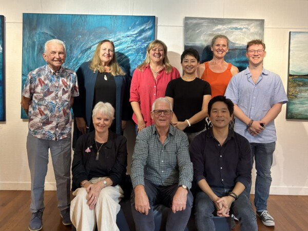 Group of nine people posing together in an art gallery with paintings on the wall.