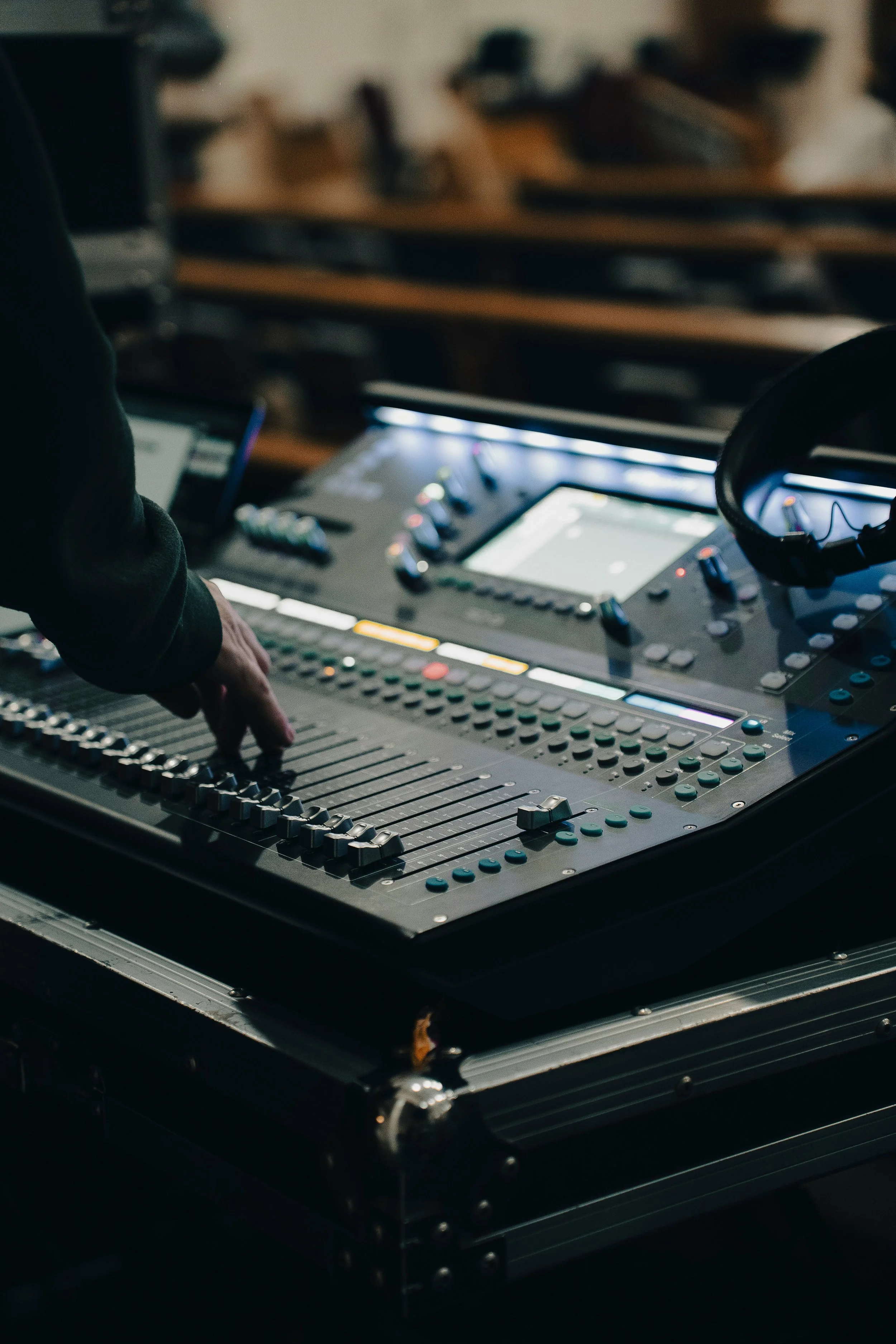 Close-up of DJ mixing console with a person's hand adjusting a slider, headphones resting on the console, in a dimly lit setting.