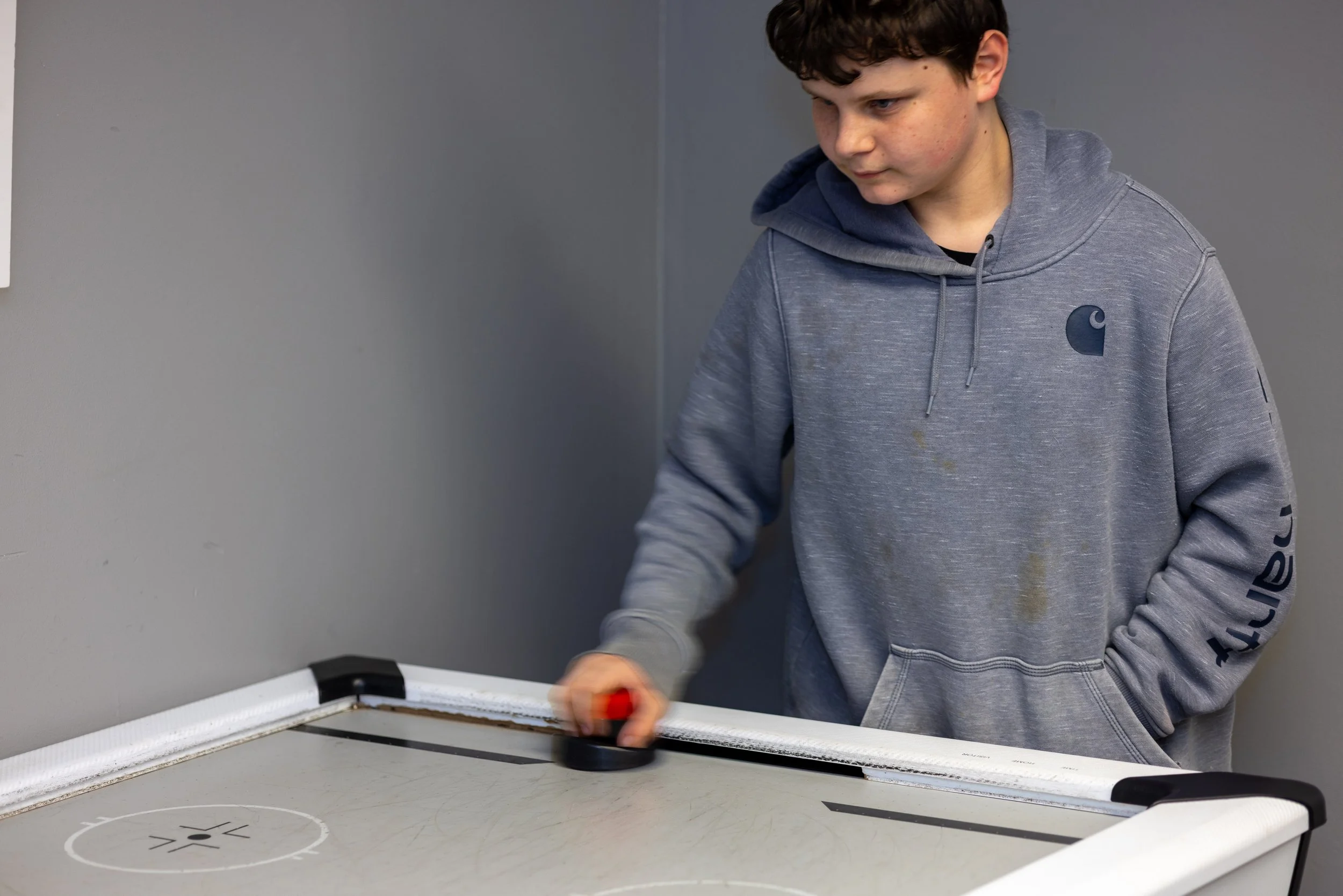 A young man playing air hockey at a table in an indoor setting.