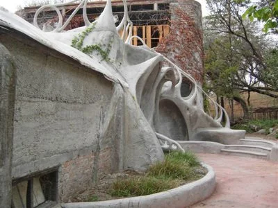Concrete sculpture of a dragon or serpent, part of an outdoor artistic installation with steps and trees.