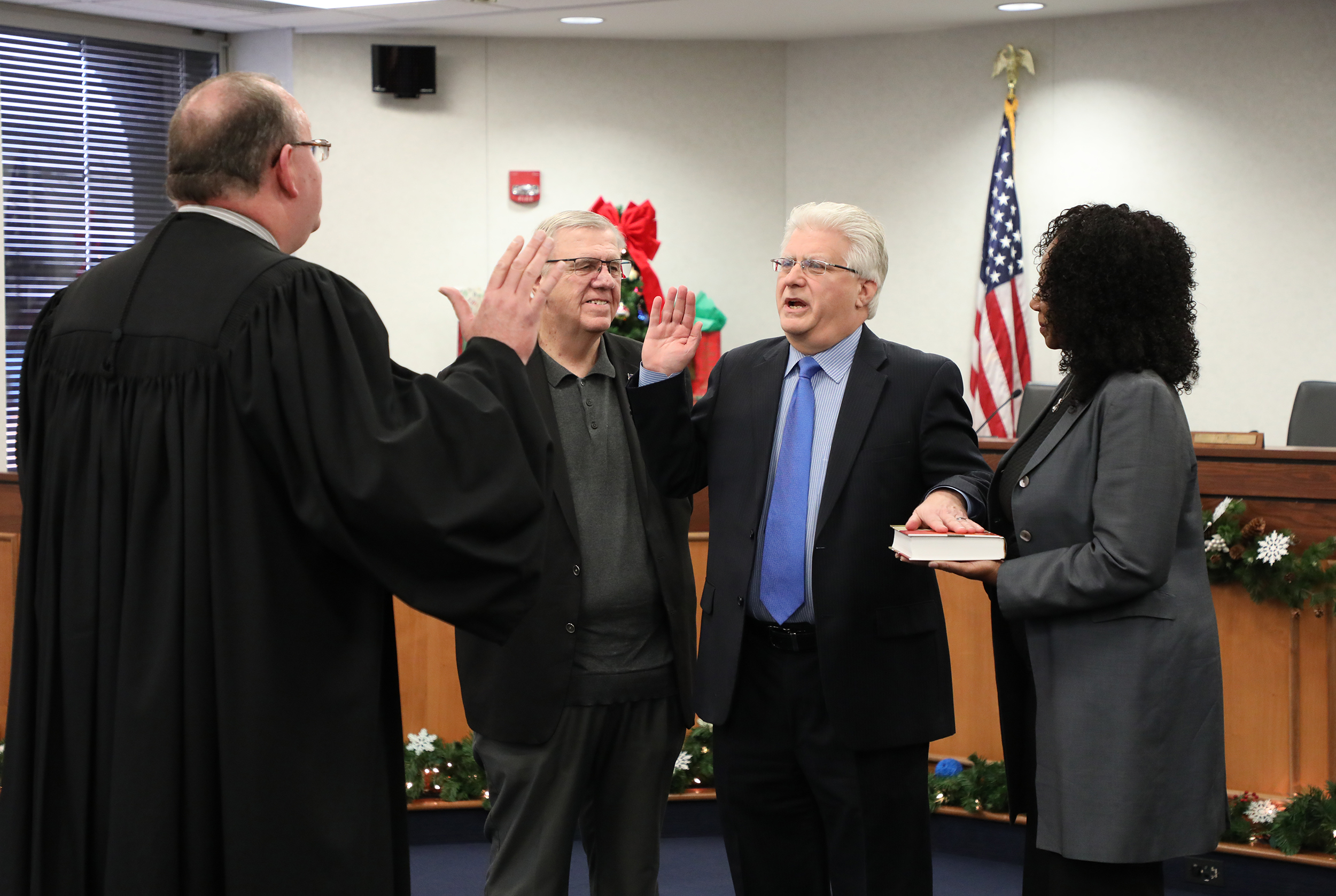 A courthouse scene with a judge swearing in Matt Lundy while a woman holds a book and another man gestures.