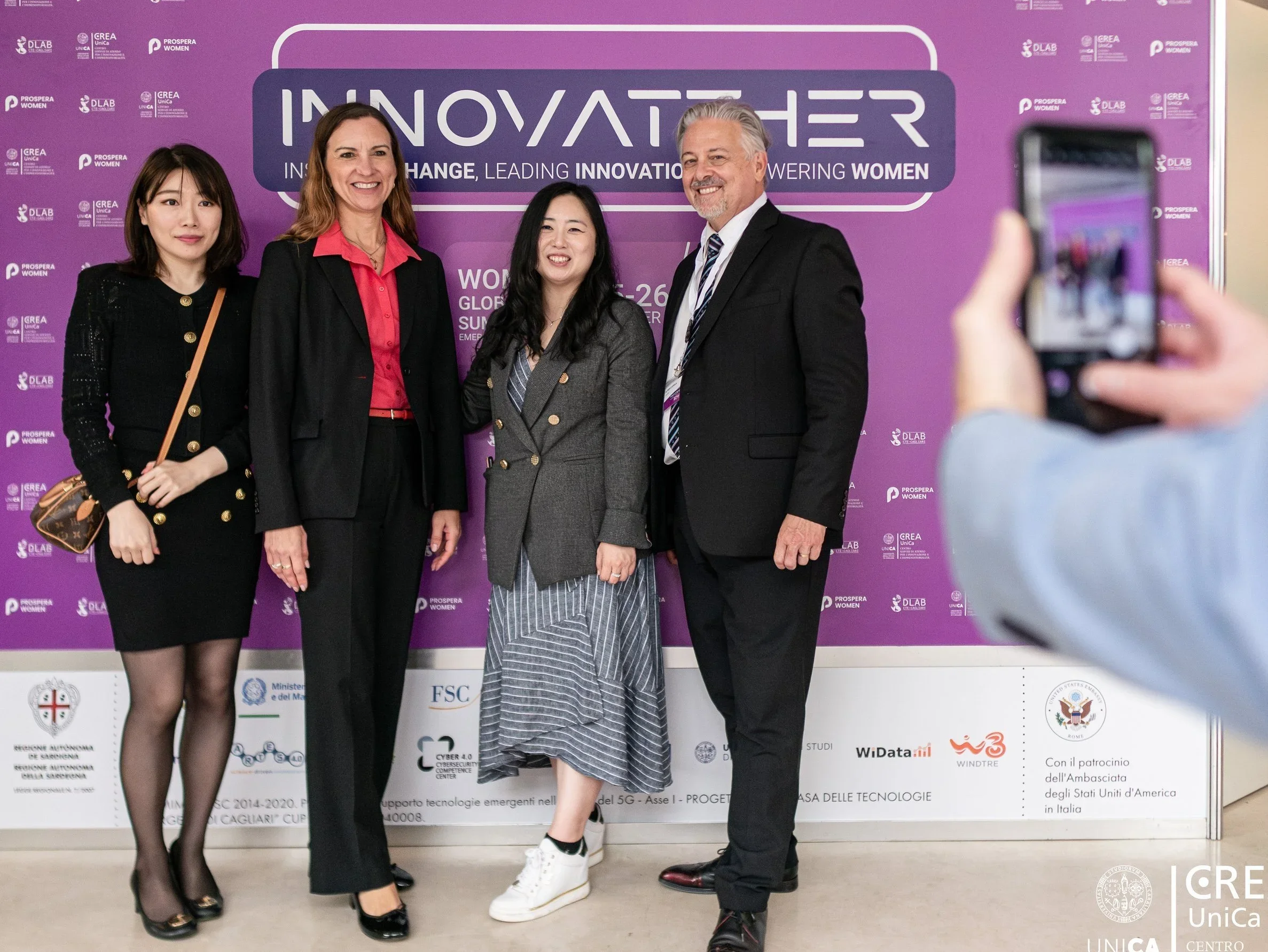 Four people standing in front of a purple event backdrop at an innovation conference, taking a group photo.