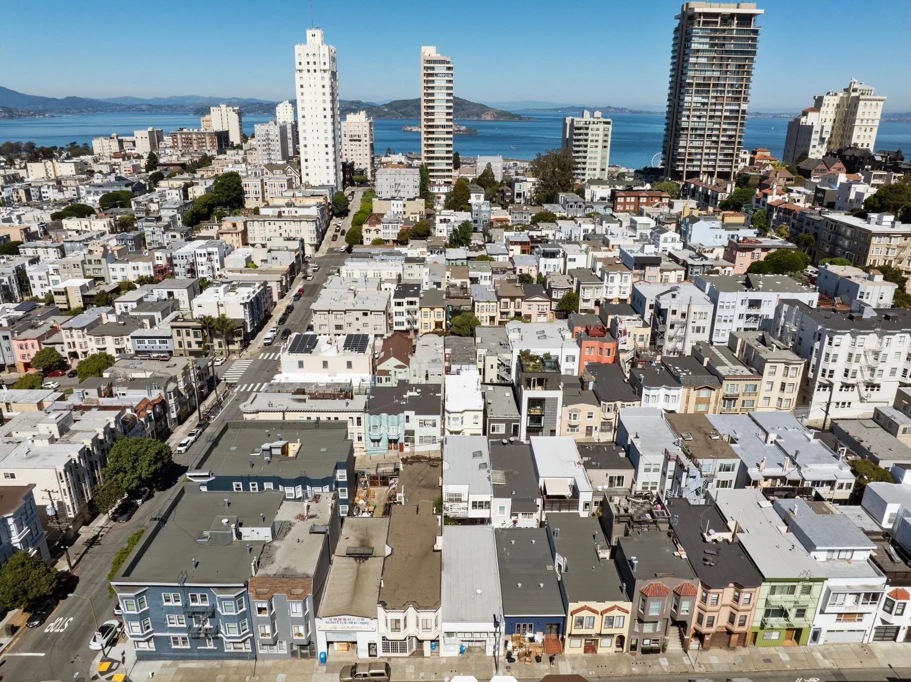 Aerial view of a city with a mix of low-rise and high-rise buildings near the water, with mountains in the background.