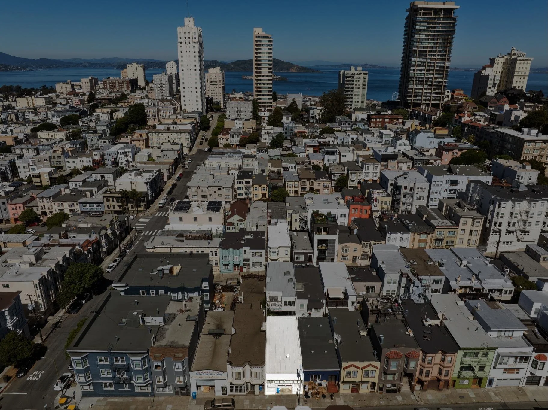 Aerial view of a city with numerous tightly packed houses and tall buildings near a body of water, with hills in the background.