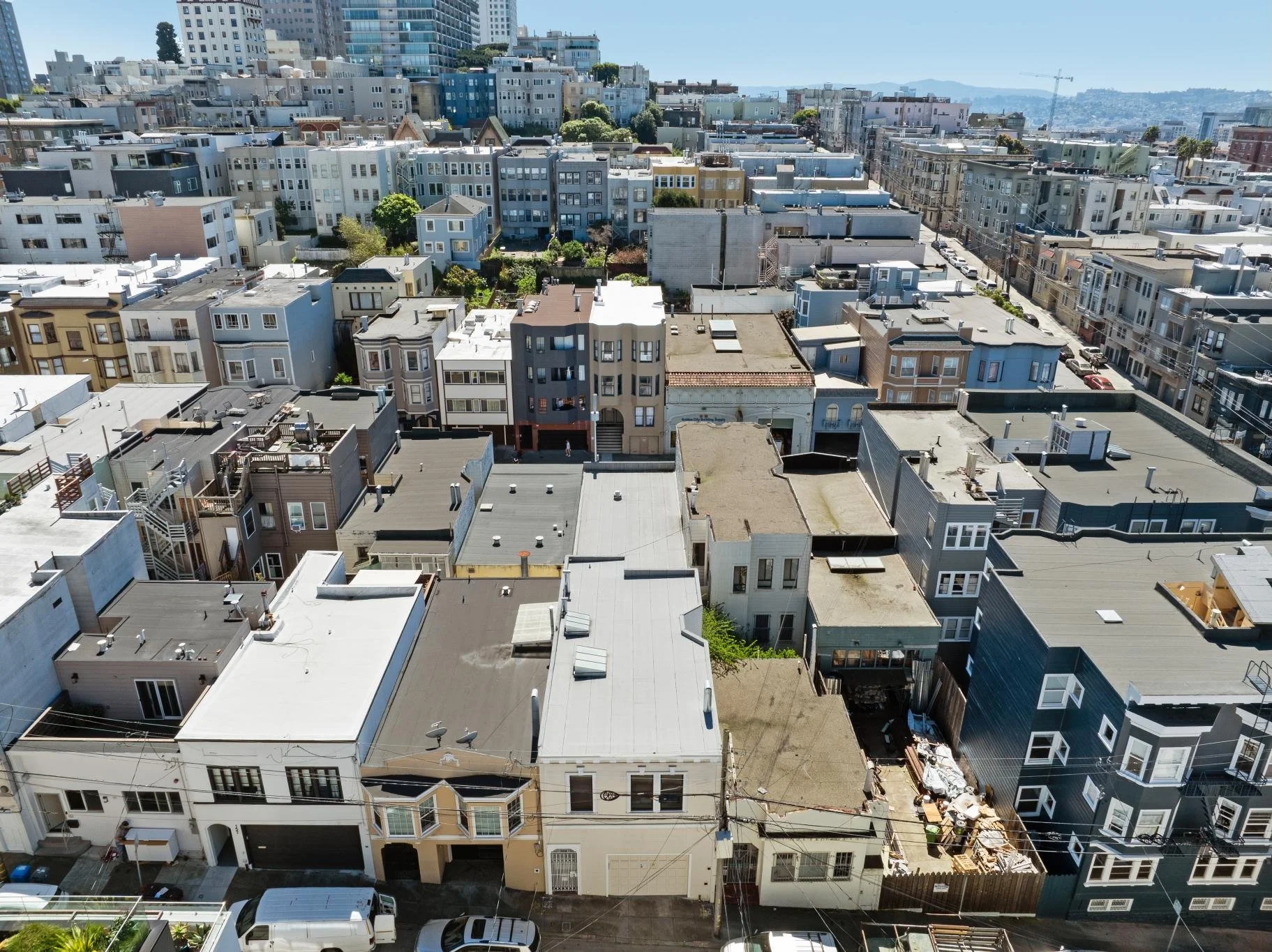 Aerial view of a densely packed urban neighborhood with various residential buildings, rooftops, and streets, under a clear blue sky.