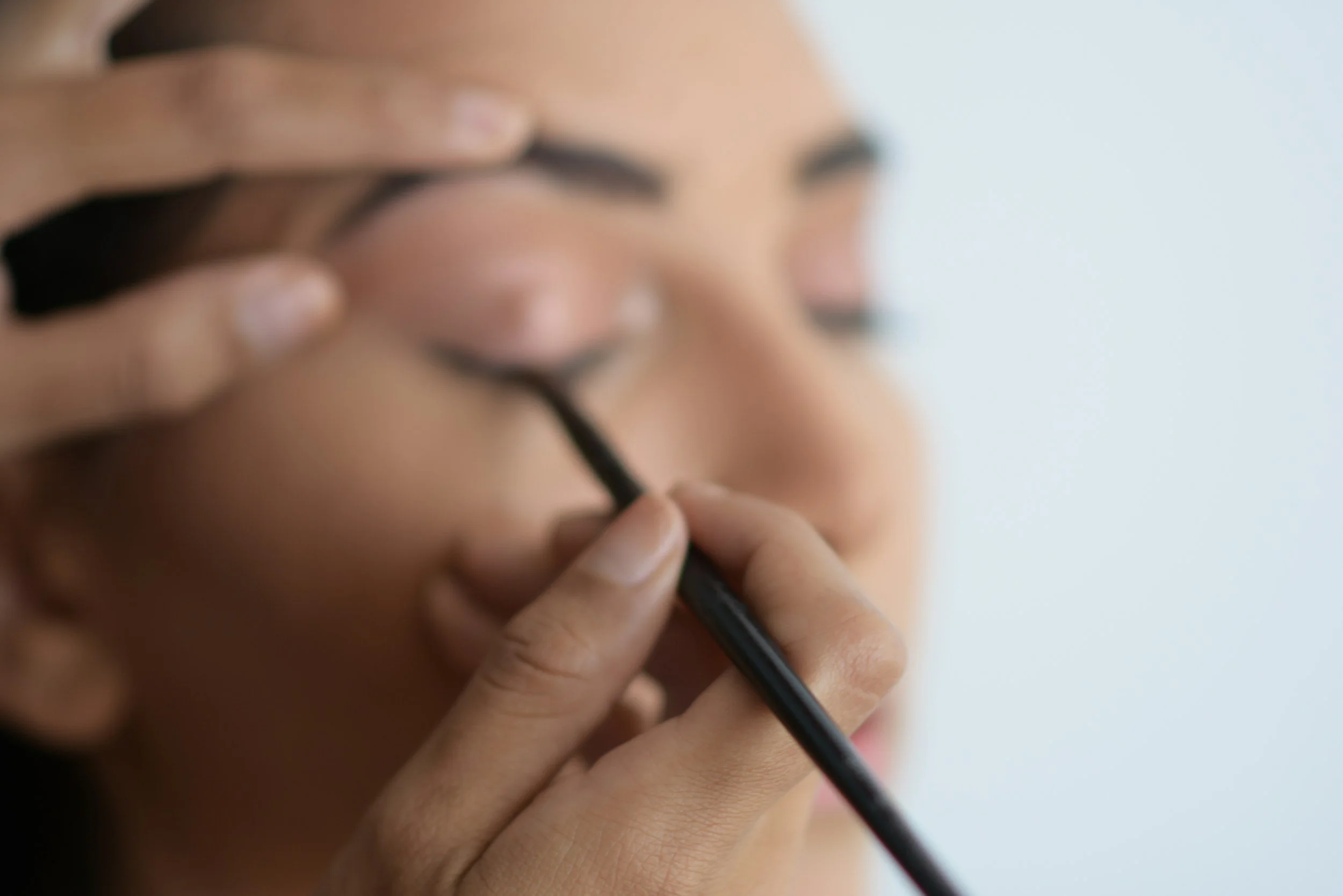 Close-up of a woman applying makeup with a brush, focusing on her face and hand, blurred background.