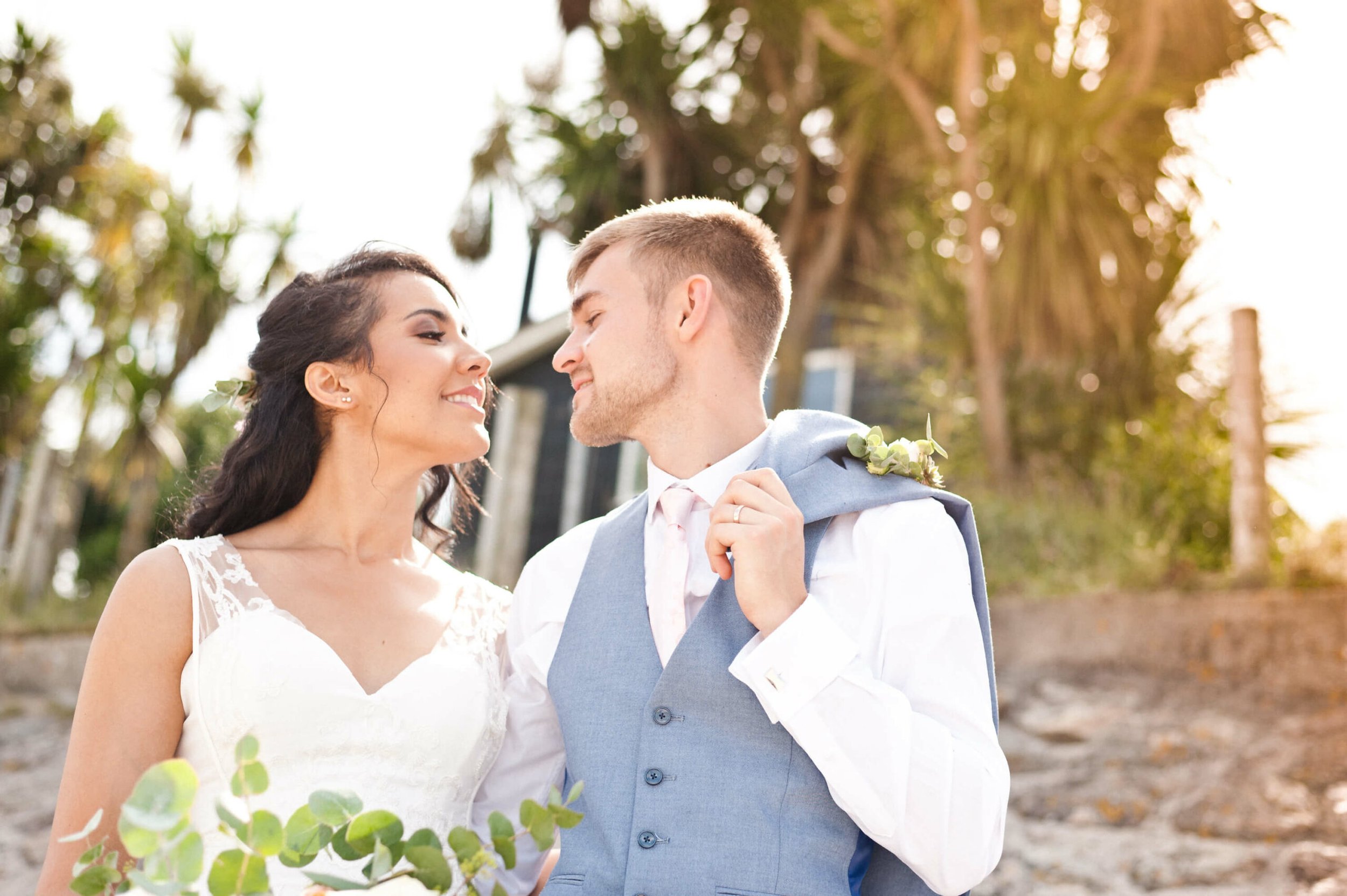 A couple on their wedding day, smiling and close to each other outdoors during golden hour in a natural setting with trees.