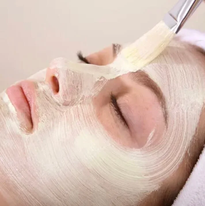 Close-up of a woman with eyes closed getting a facial mask applied with a brush.