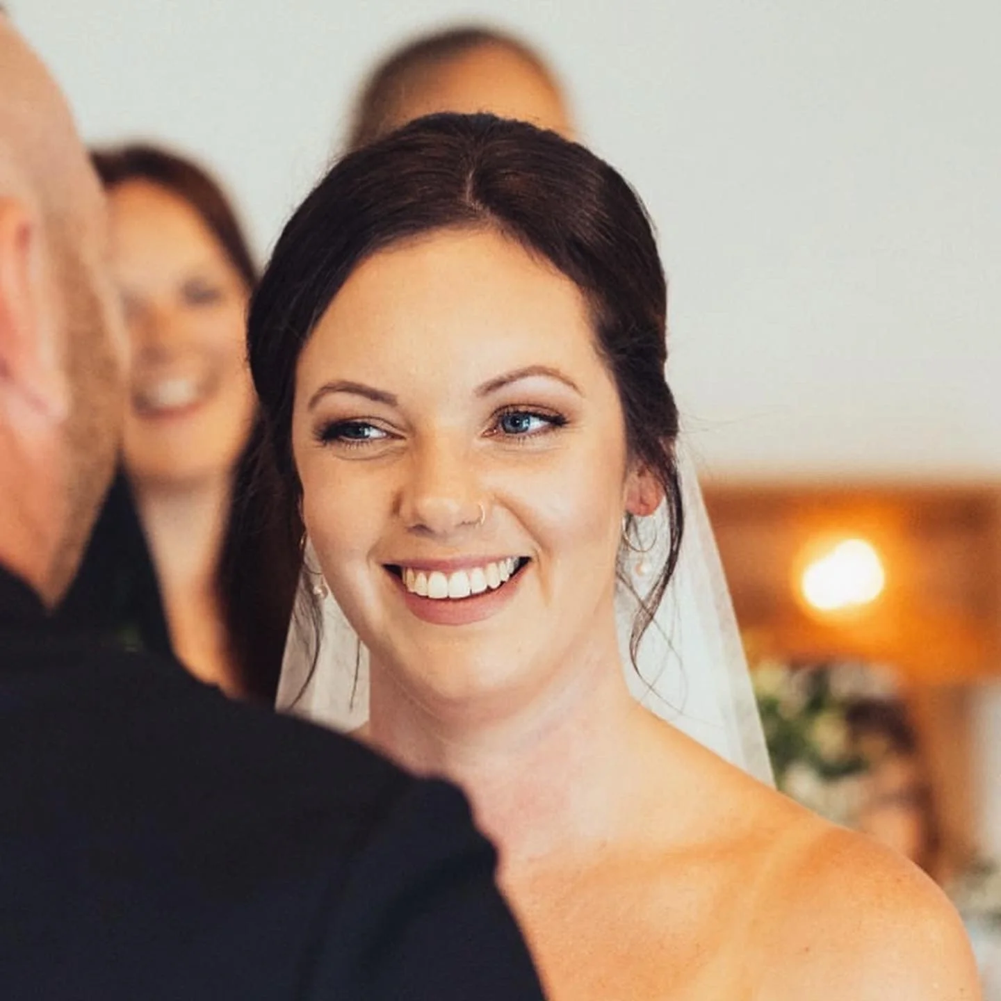 A smiling bride with dark hair and blue eyes during her wedding ceremony.