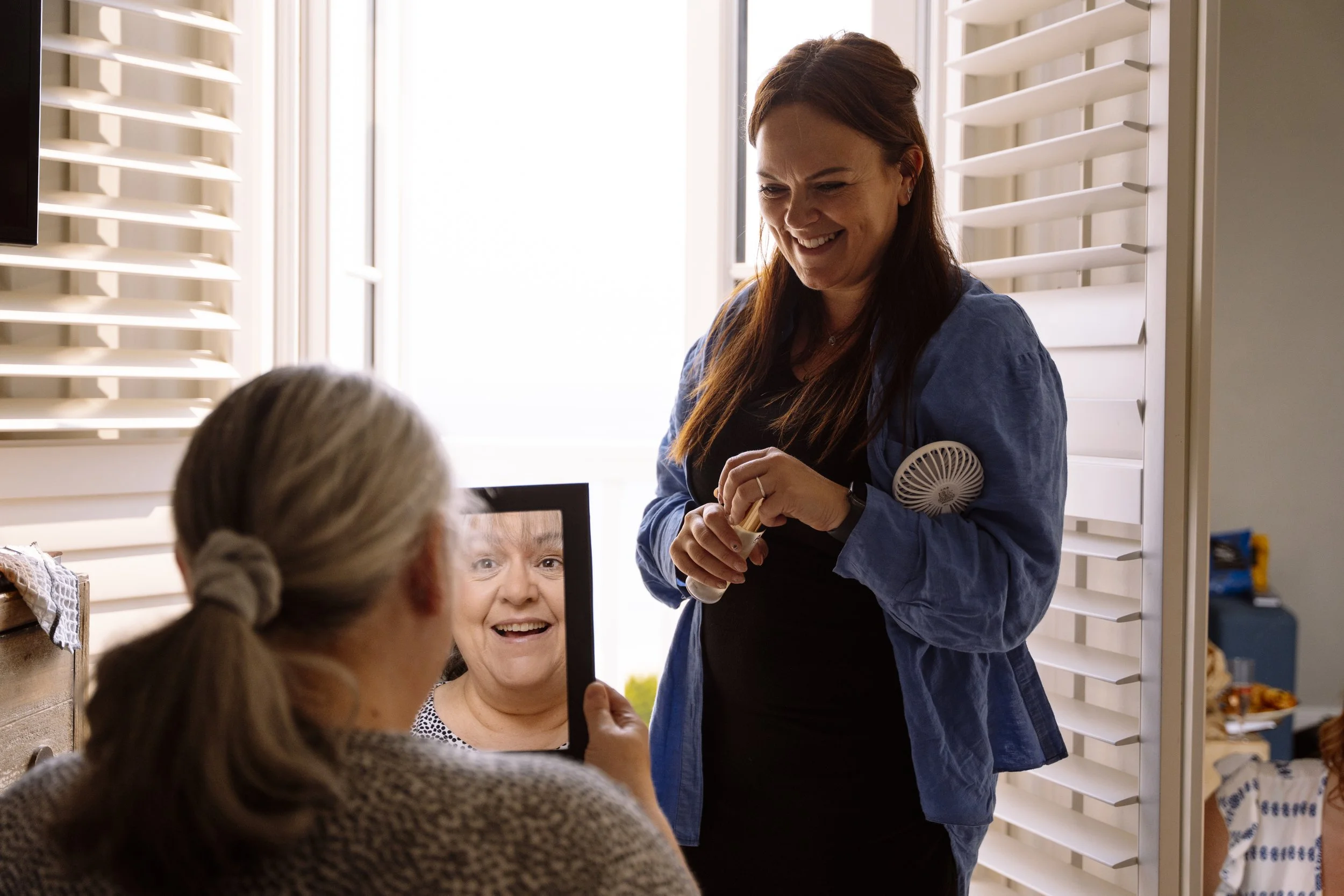 Denise Jackson smiles as she talks to a client at a gathering inside a well-lit room with white shutters and shelves.