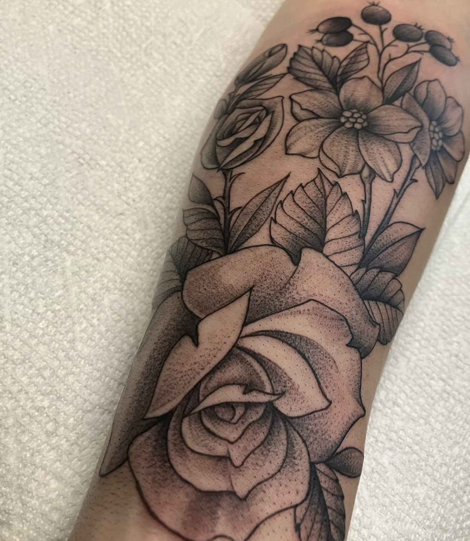 A tattoo featuring detailed black and gray flowers, including roses and other blossoms, with leaves and shading.