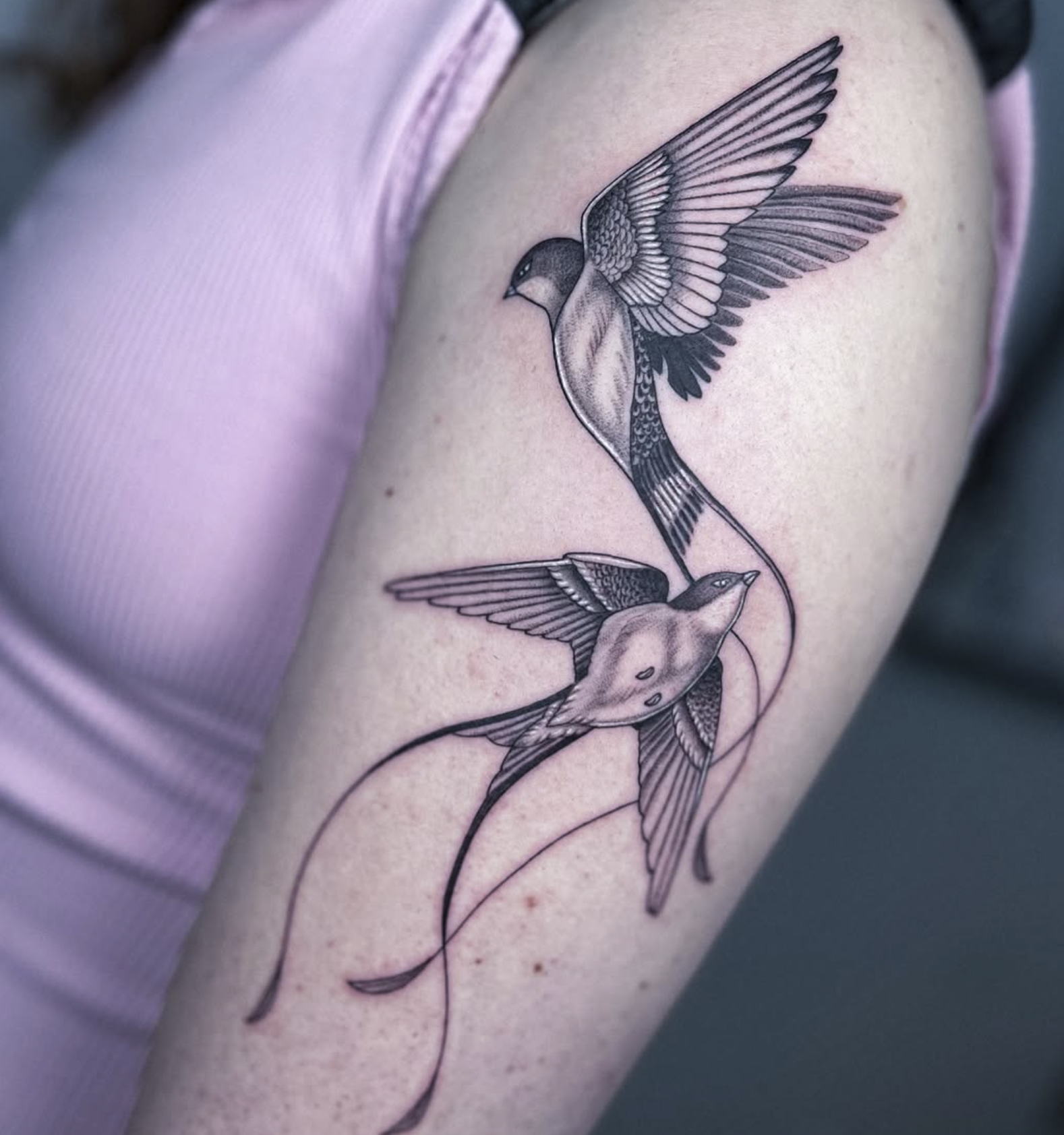 Tattoo of two birds with long tail feathers on an arm.
