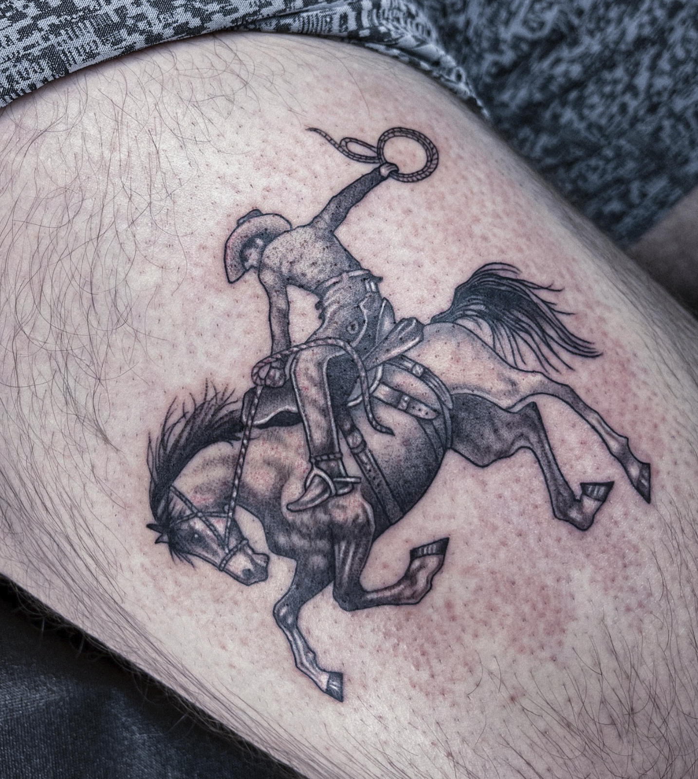 Tattoo of a cowboy riding a bucking horse with a lasso in hand.