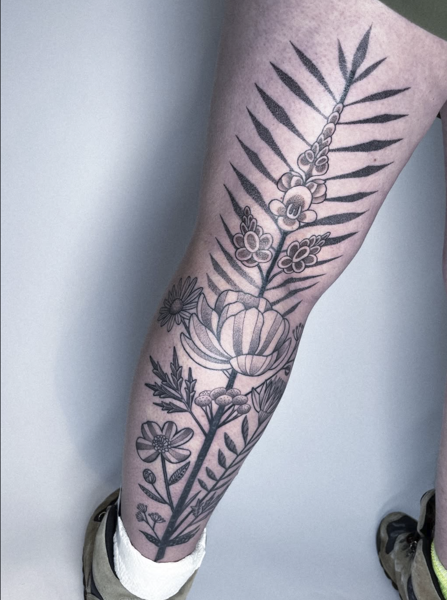 A person's leg with a large black and gray floral tattoo featuring various flowers and leaves.