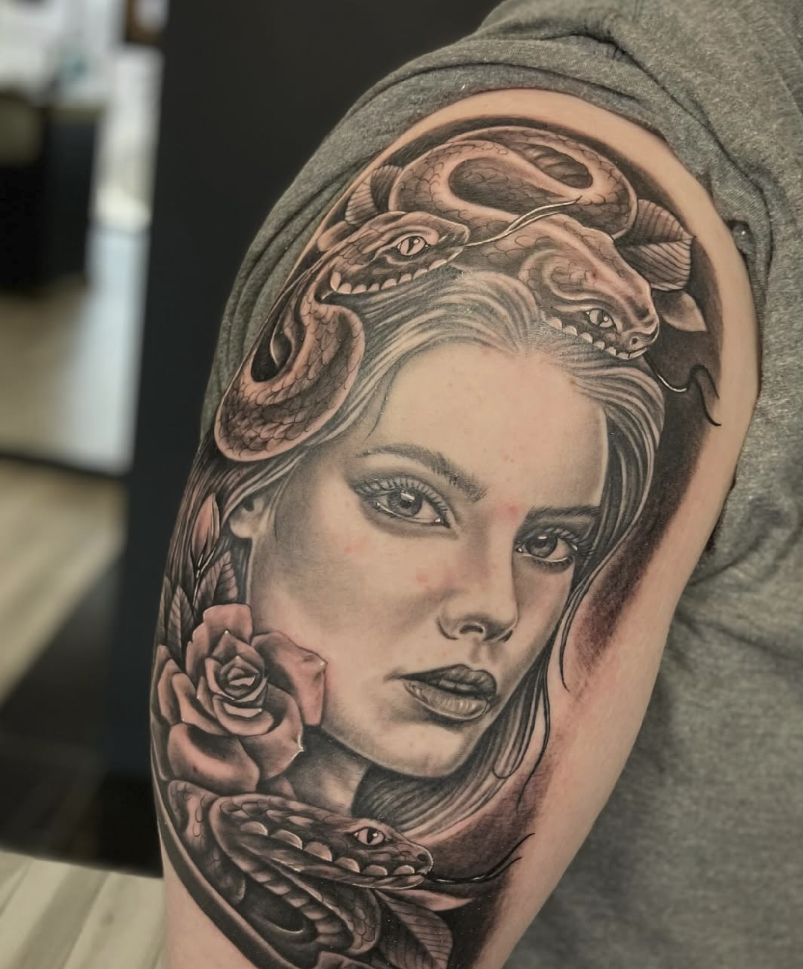 Black and gray tattoo of a woman's face with snakes, roses, and a dragon on her head.