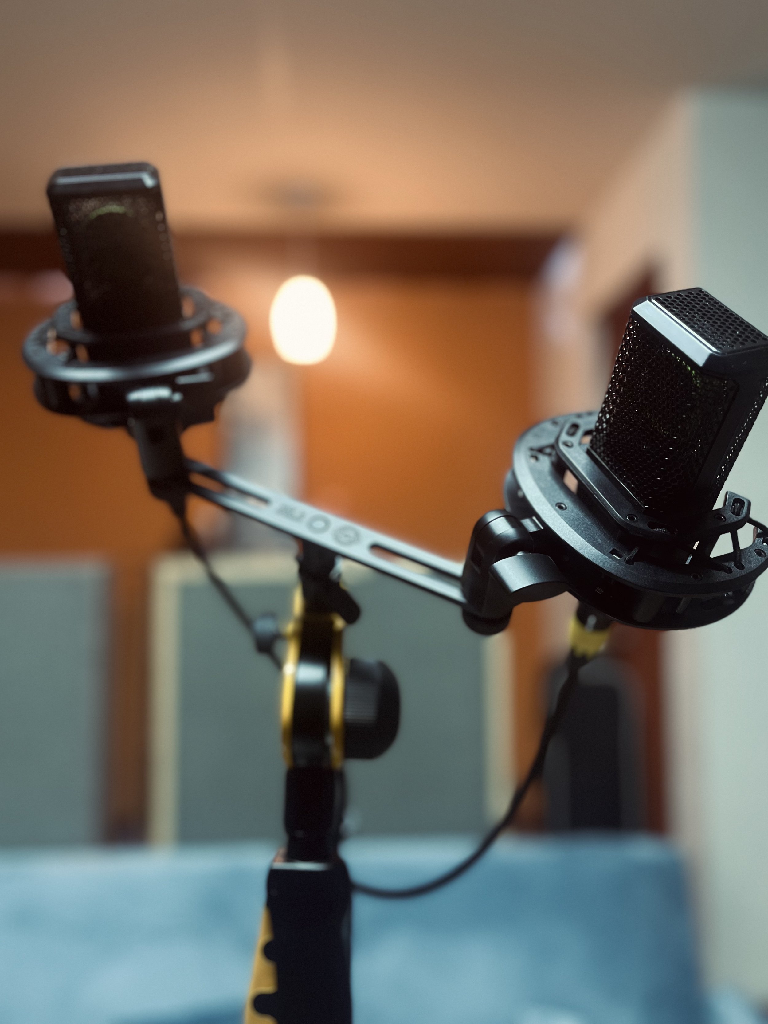 A selfie stick holding a smartphone in a room with beige walls and a ceiling light, with a slightly blurred background.