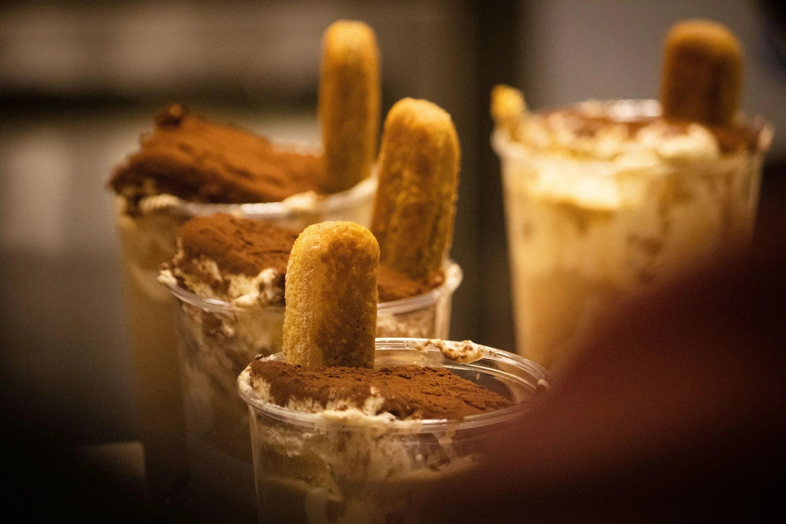 Three cups of tiramisu with ladyfingers and cocoa powder, one in the foreground and two in the background.