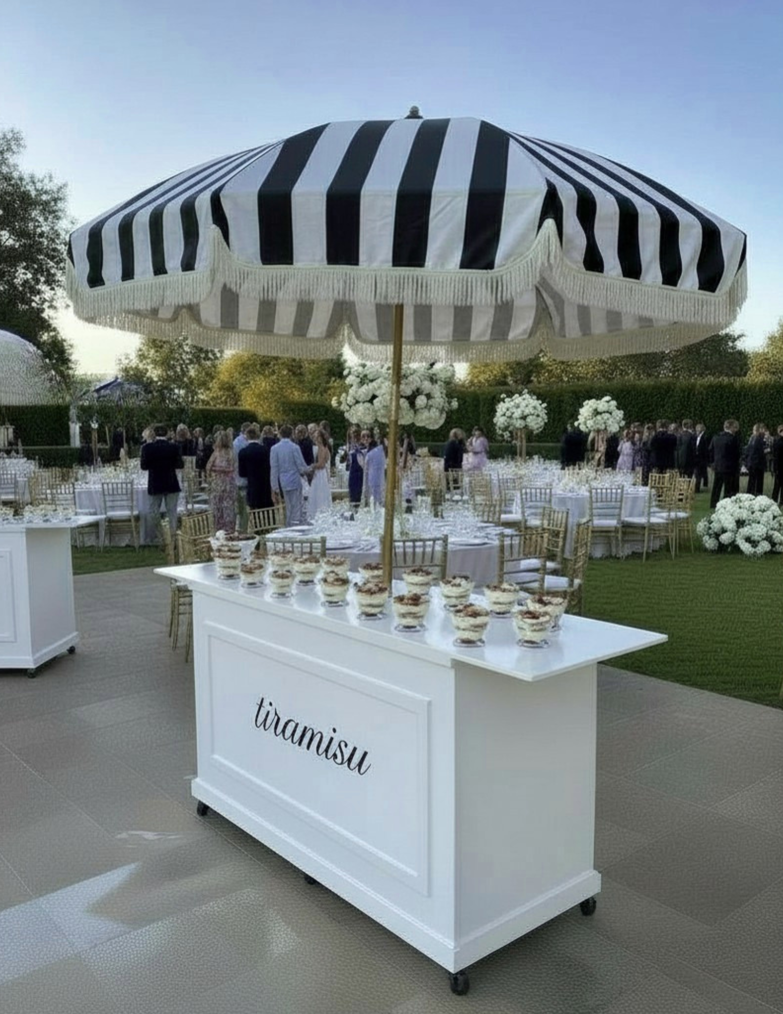 Tiramisu dessert display at an outdoor wedding reception with a black-and-white striped umbrella.
